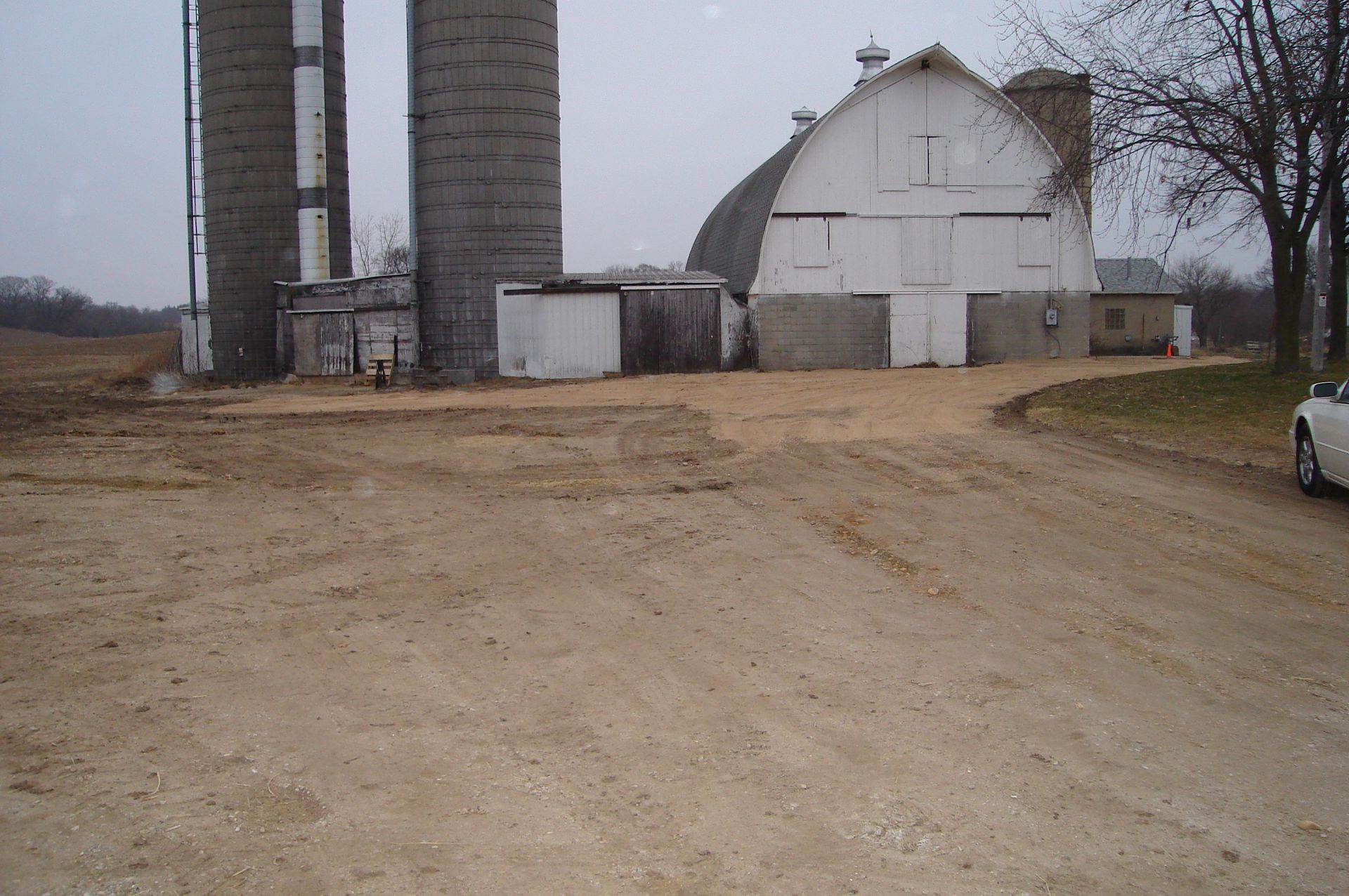 A white car is parked in front of a barn