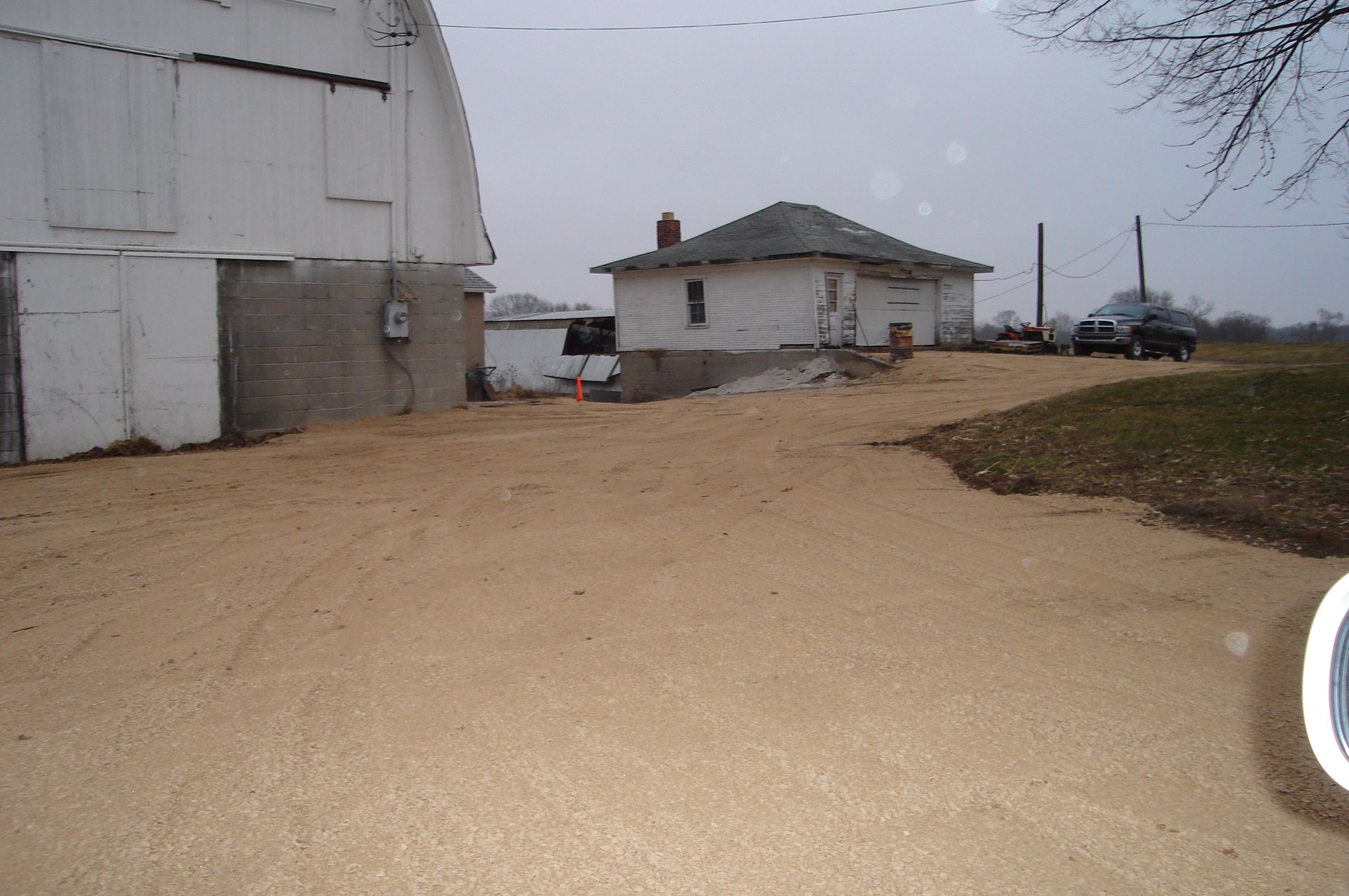 A dirt road leading to a white barn and a small house