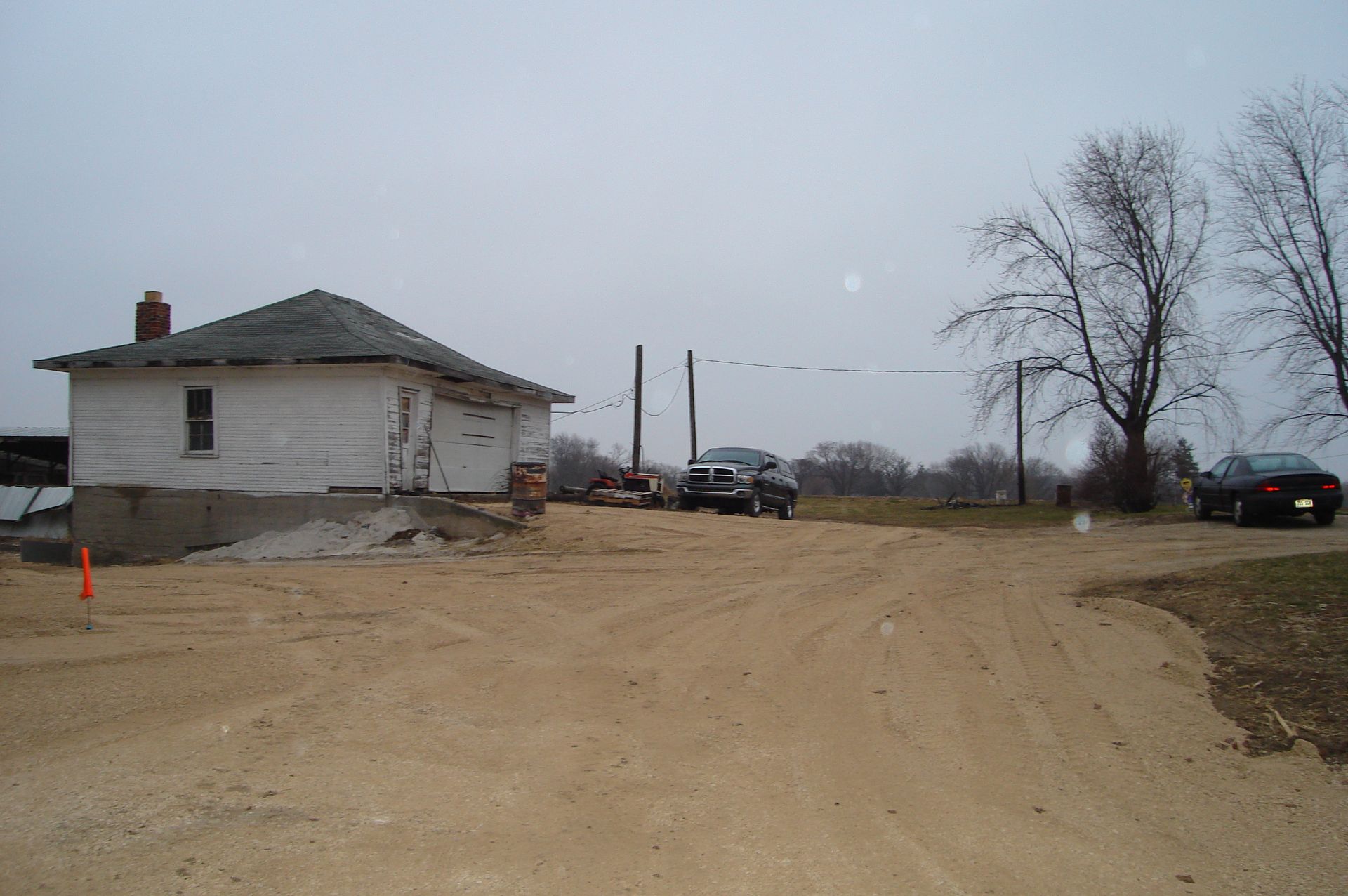 A dirt road leading to a house with cars parked in front of it