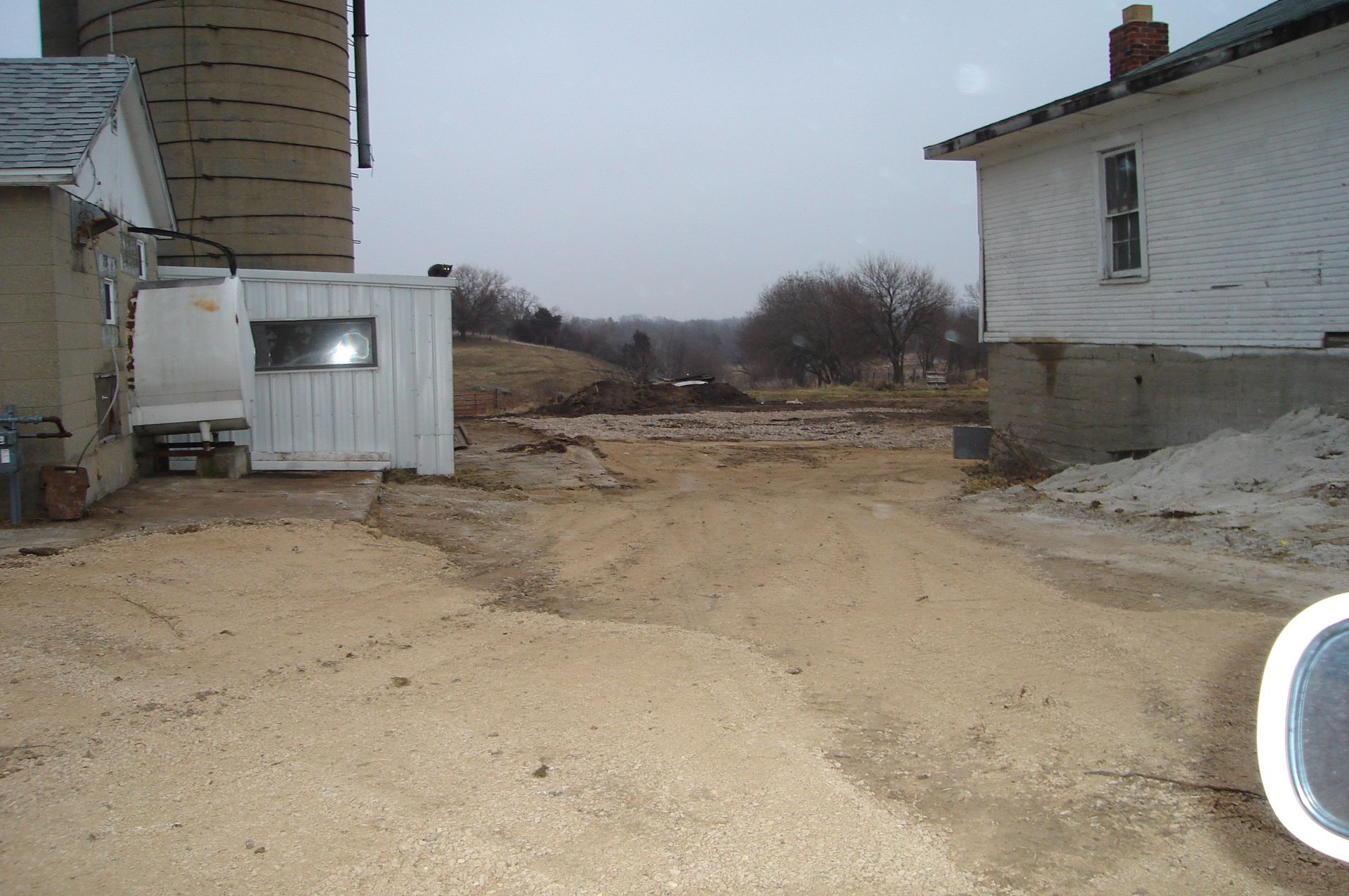 A dirt road leading to a house with a silo in the background