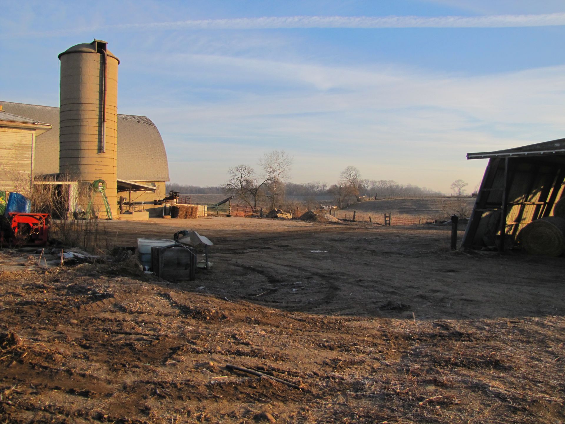 A tractor is parked in a dirt field with a silo in the background