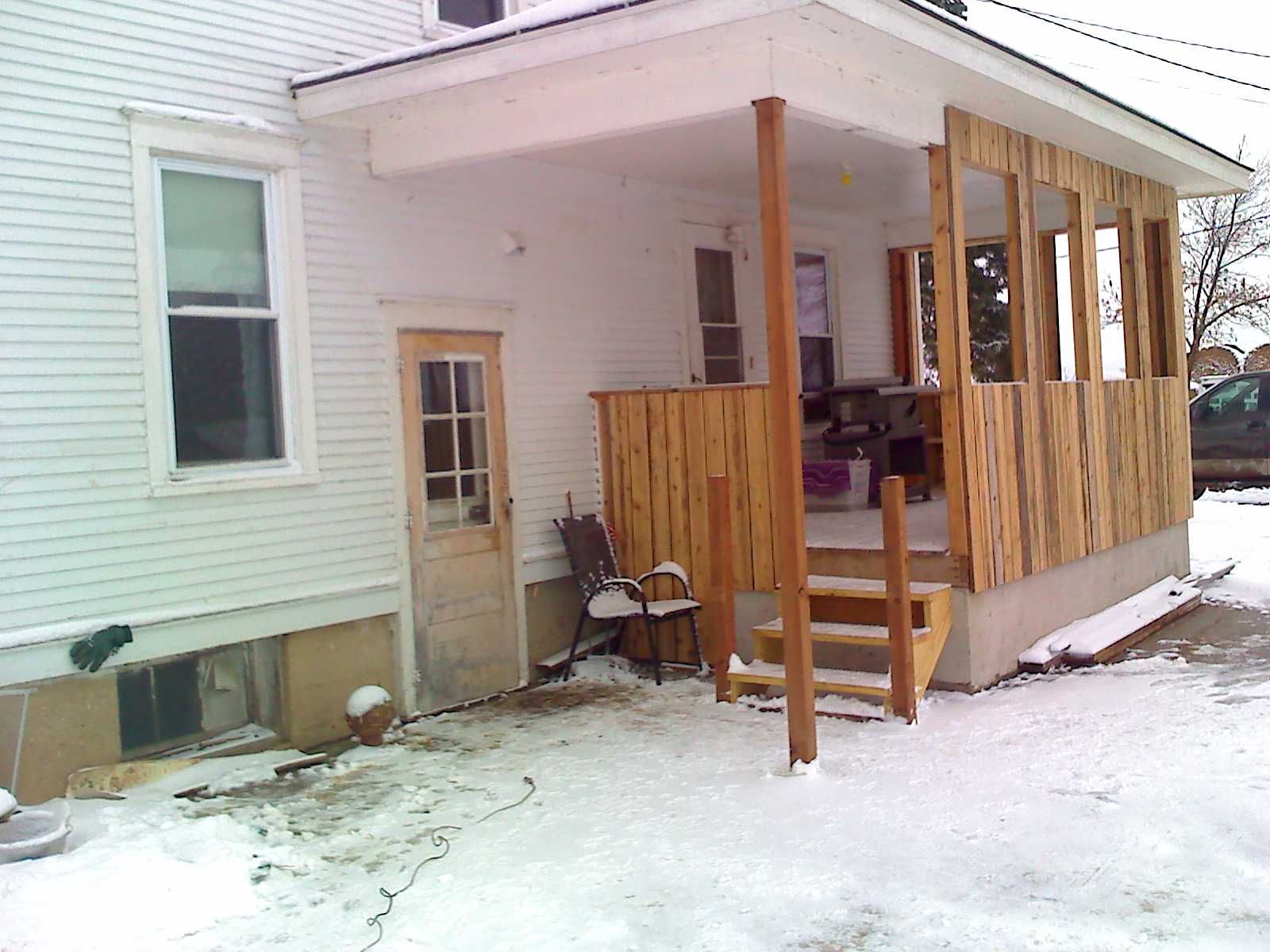 A white house with a porch and stairs in the snow