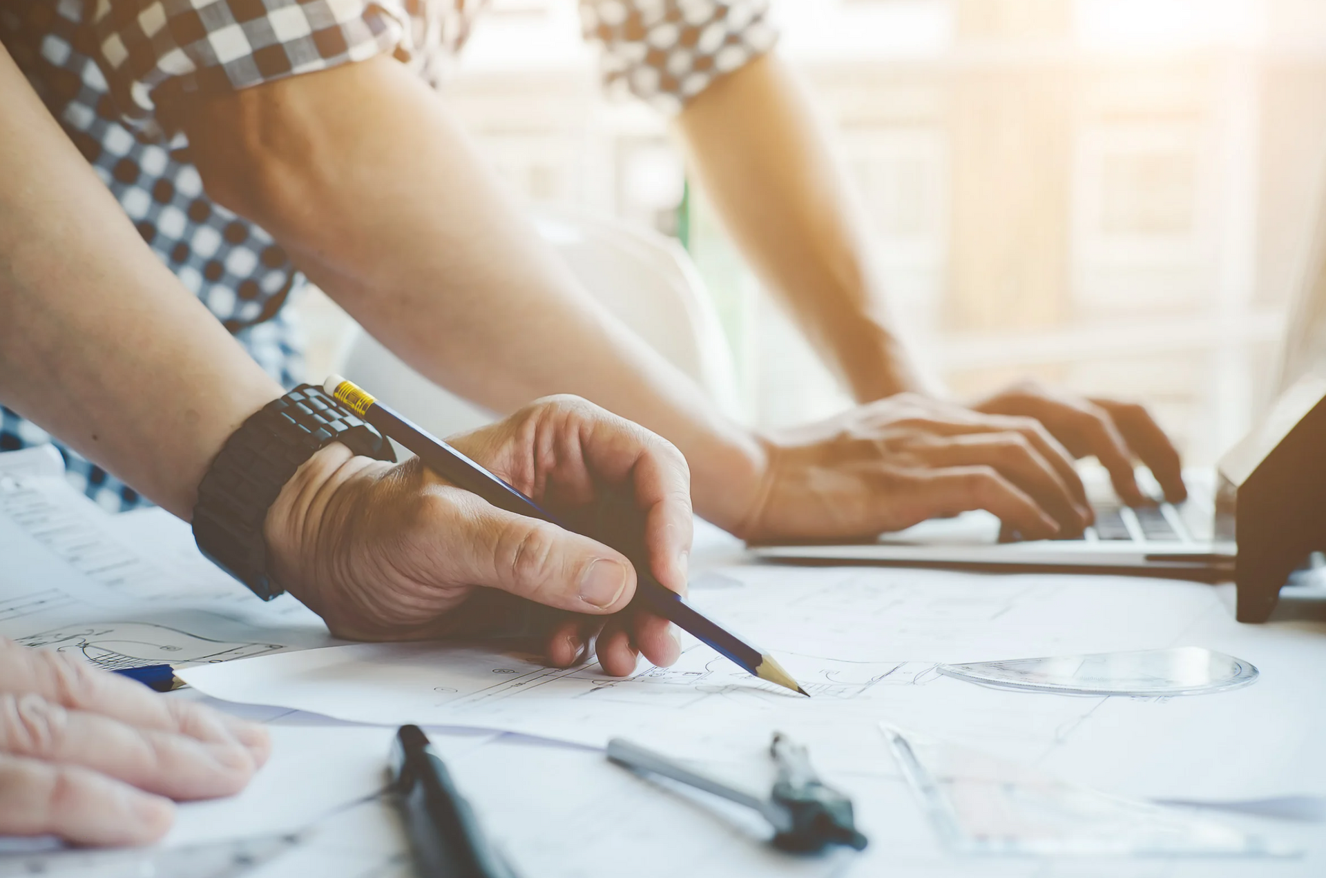 A man is writing on a piece of paper while using a laptop computer.