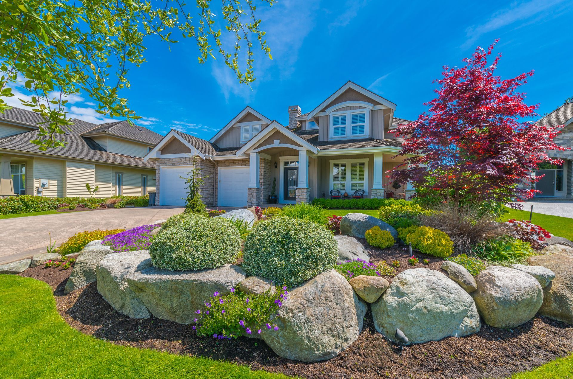 Nicely decorated front yard with flowers, stones and bushes as a decorative elements. Landscape design.