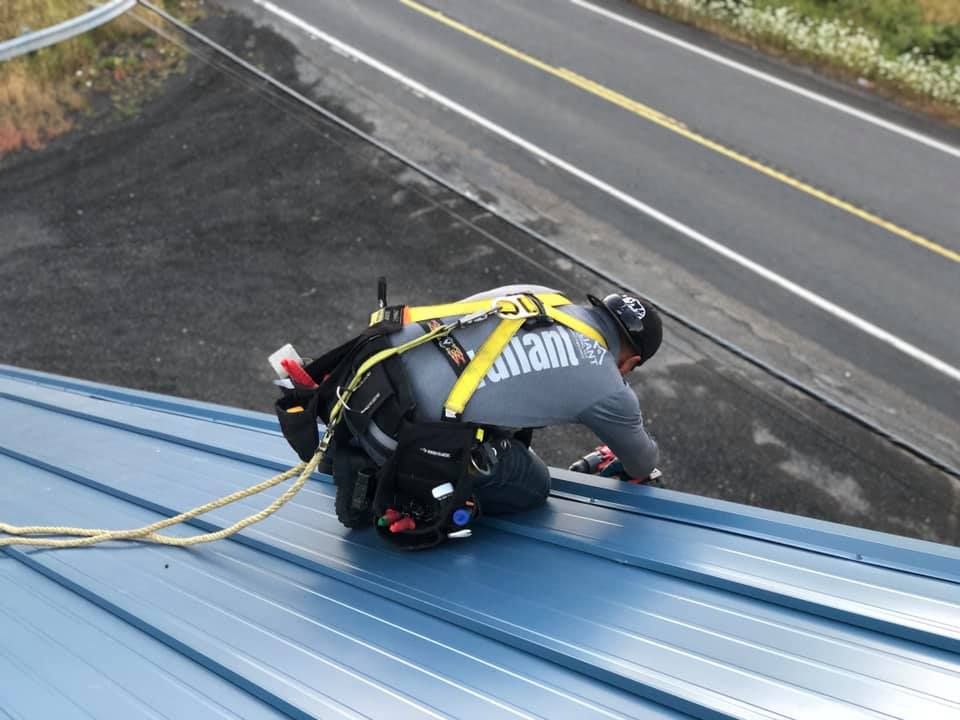 A man is kneeling on top of a blue roof.