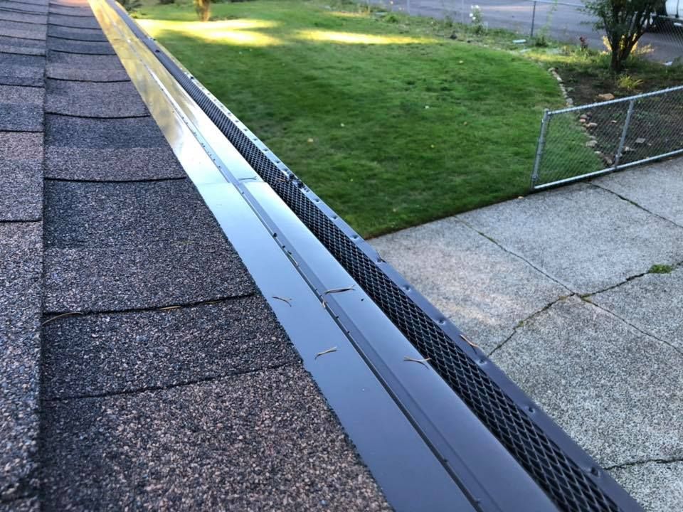 A gutter on the side of a house with a fence in the background.