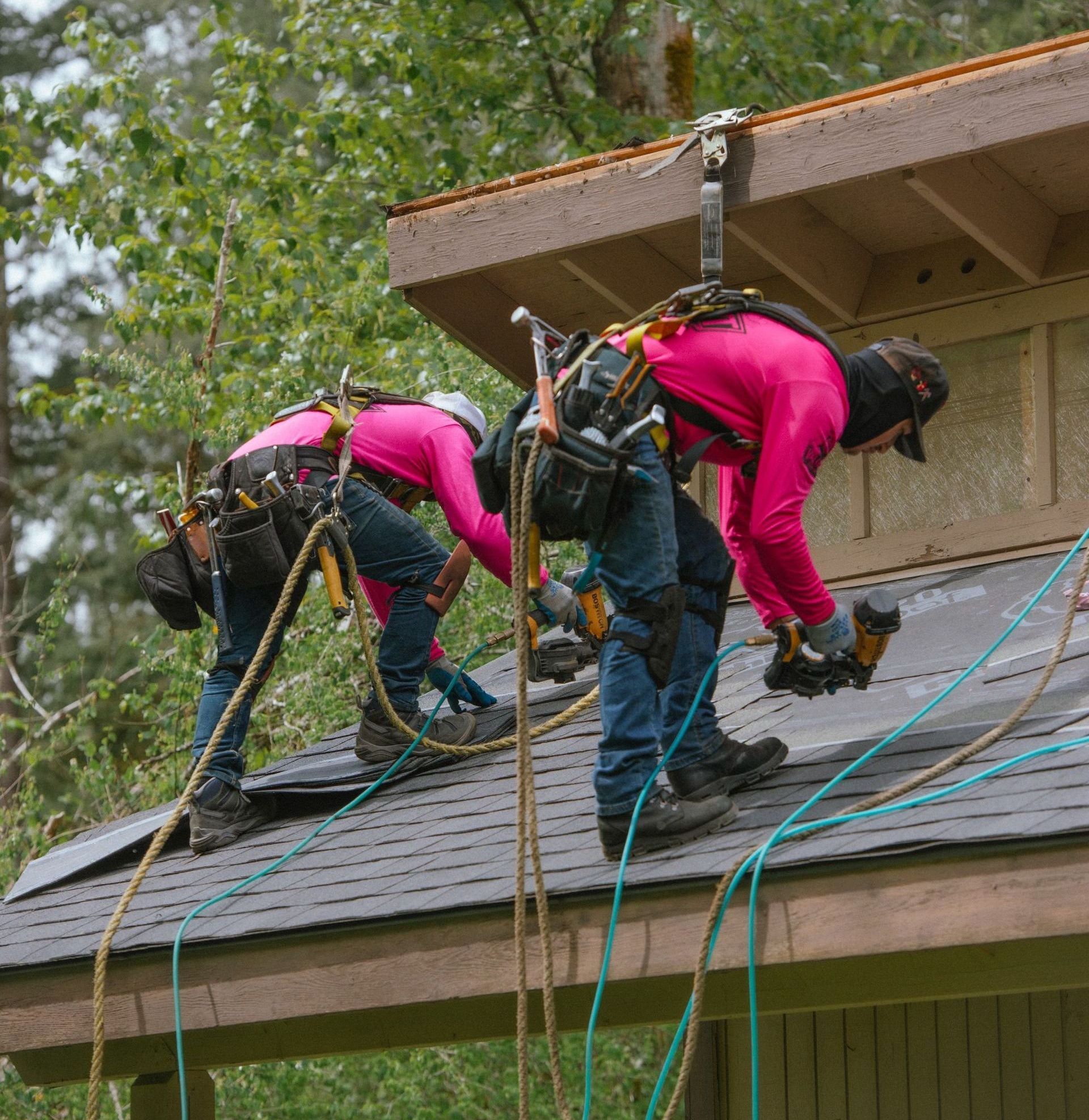 A man is standing on a roof holding a drill and smiling.