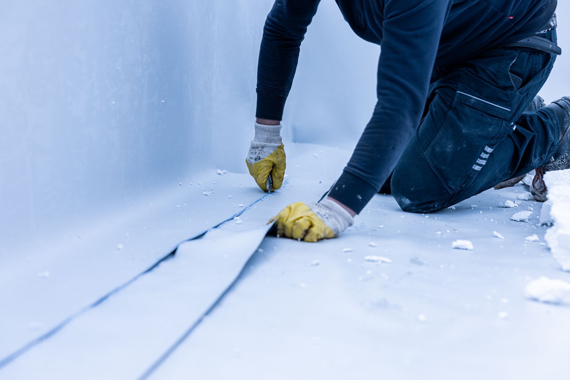 A man wearing yellow gloves is kneeling down on a white surface.