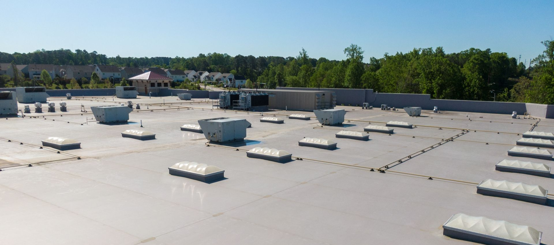 View of a flat commercial roof with skylights, vents, and HVAC units, trees and buildings in the background.