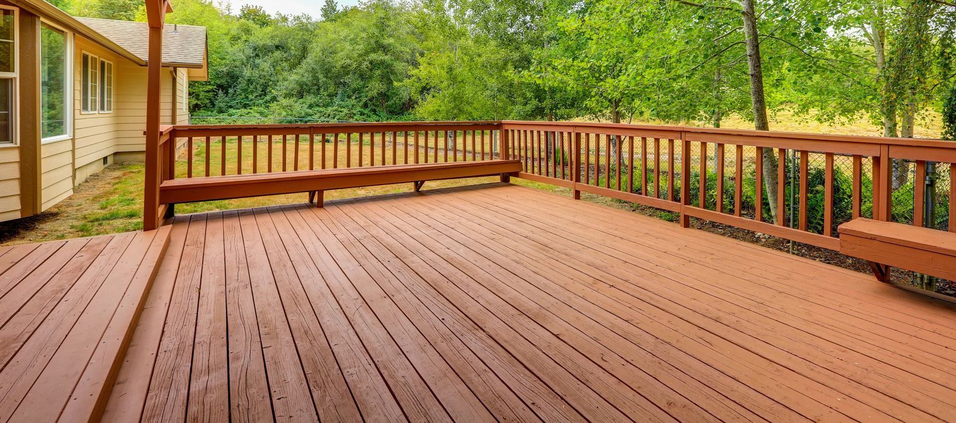 A large wooden deck with a railing and benches in front of a house.