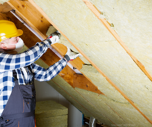 A man wearing a hard hat and overalls is working on a roof.