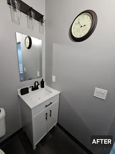 Small renovated bathroom with white vanity, gray walls, and a clock.