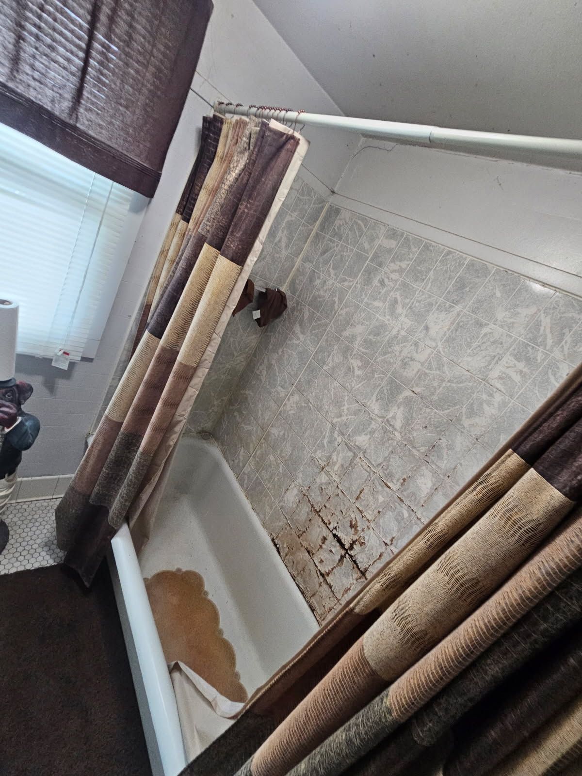 Bathroom with a tub, shower curtain, and water stains on the wall and in the tub.
