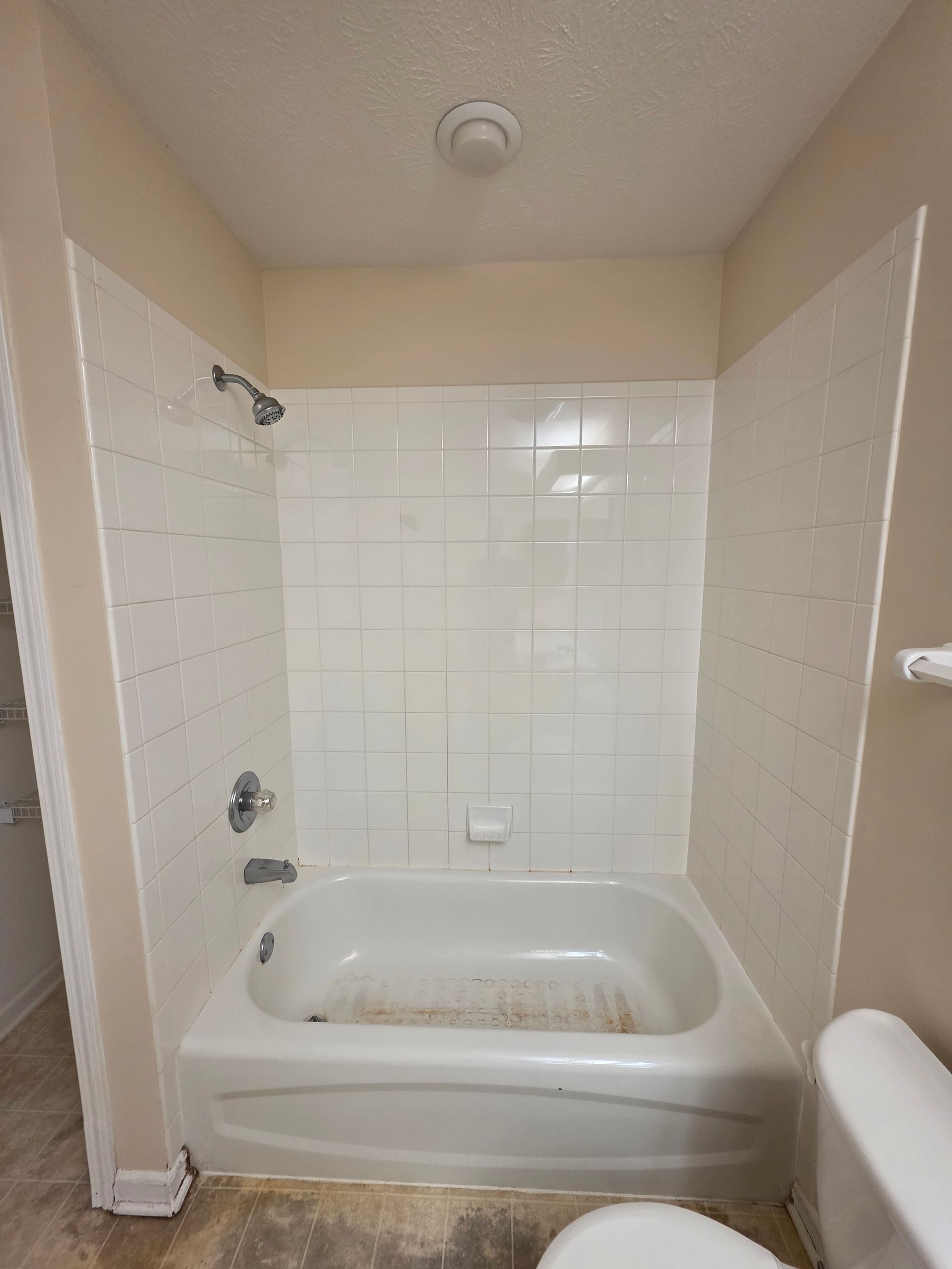 White tiled bathtub and shower with beige walls.