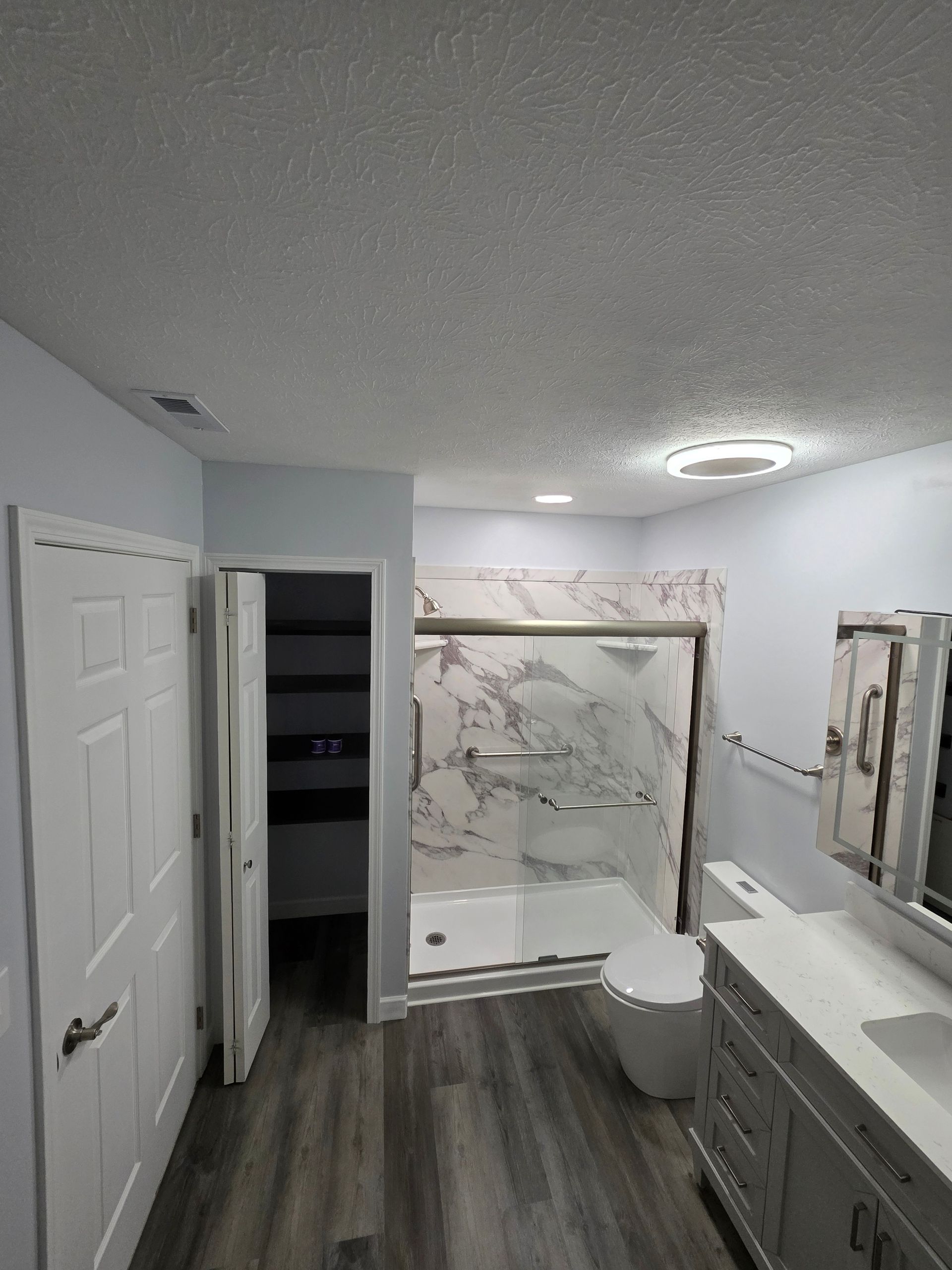 Bathroom with white cabinets, marble shower, and gray flooring.