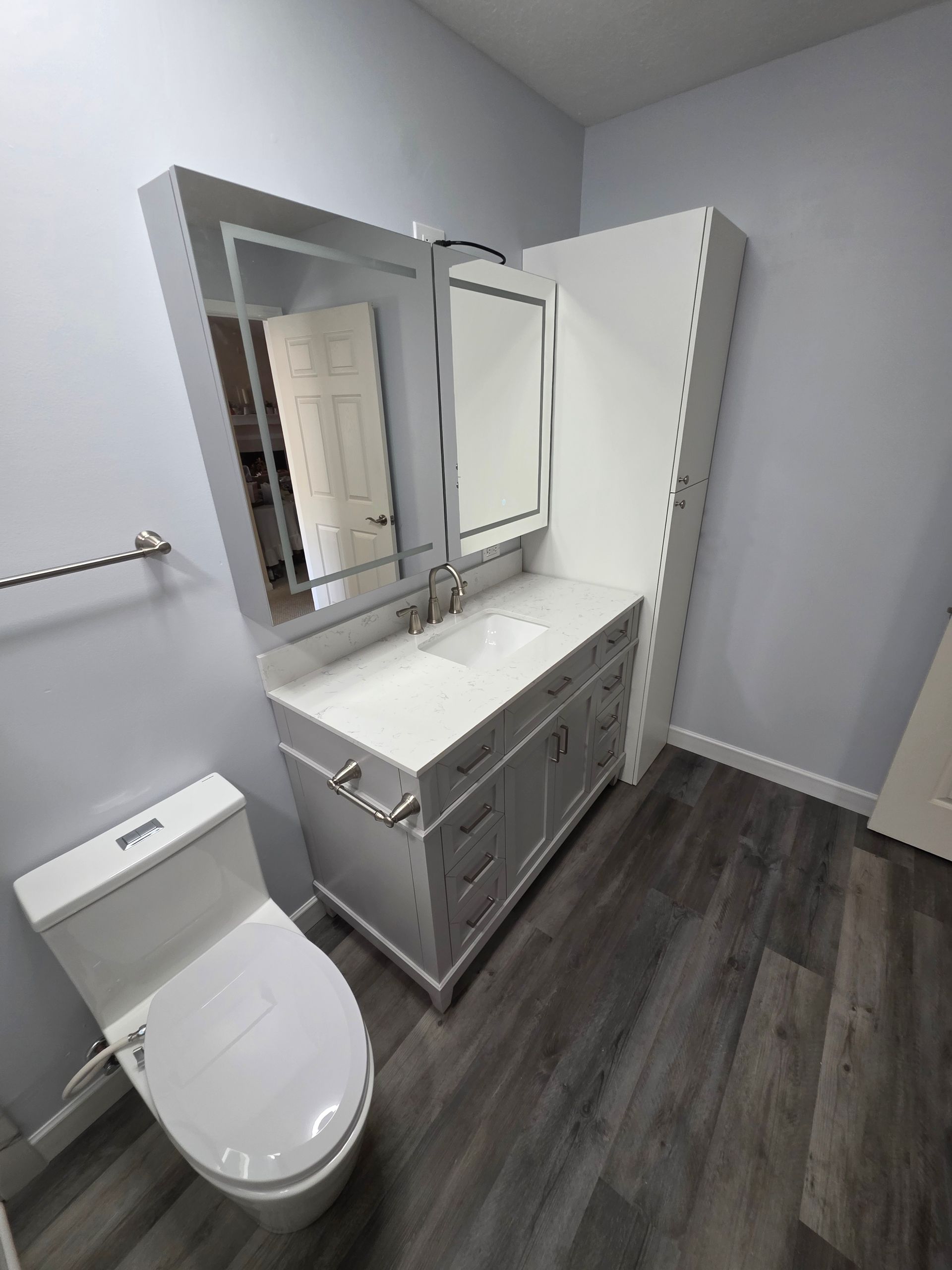 White bathroom with toilet, vanity, and mirror, against blue wall and gray floor.