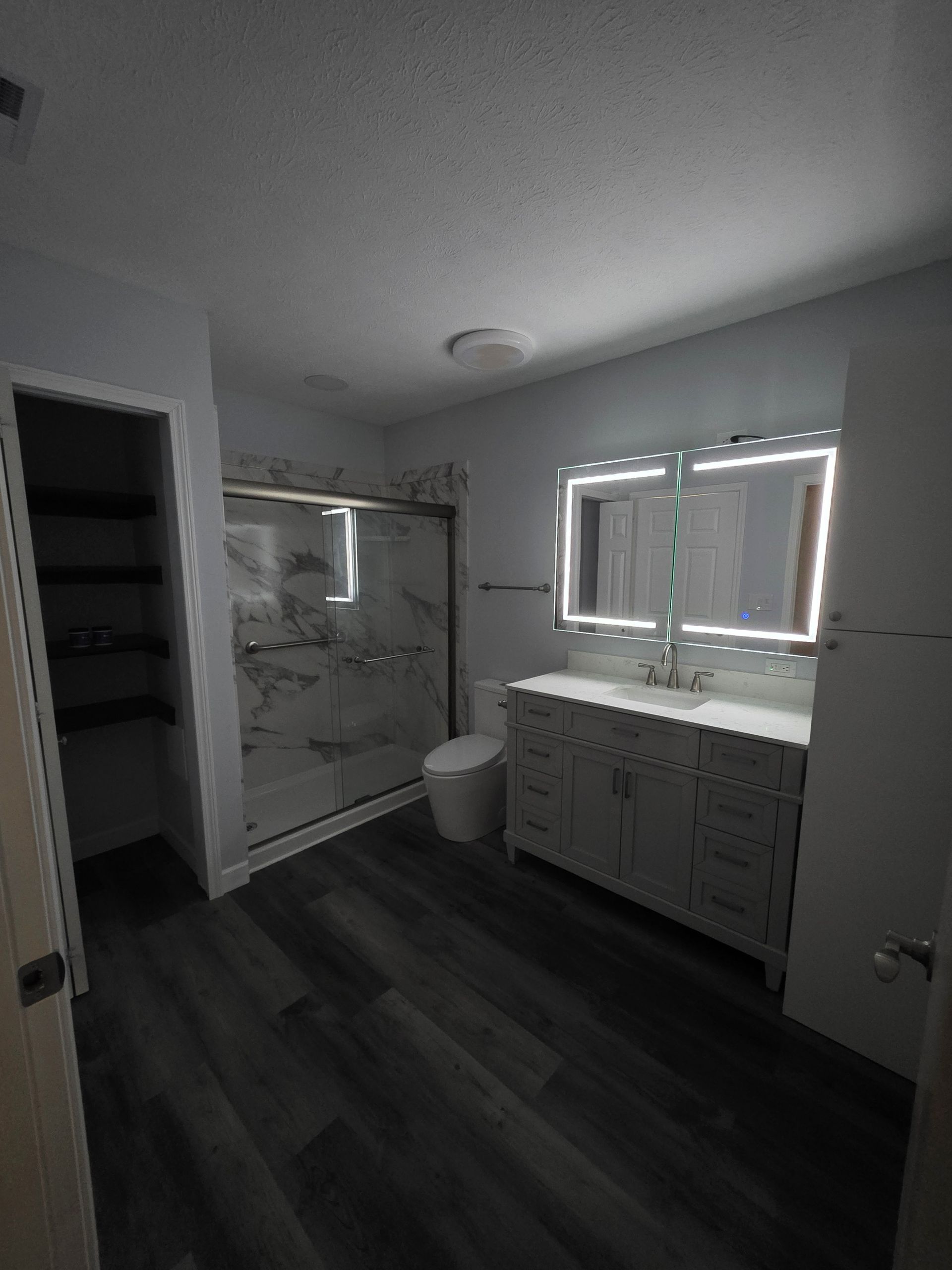 Bathroom with white vanity, large mirror, shower, and dark gray flooring.