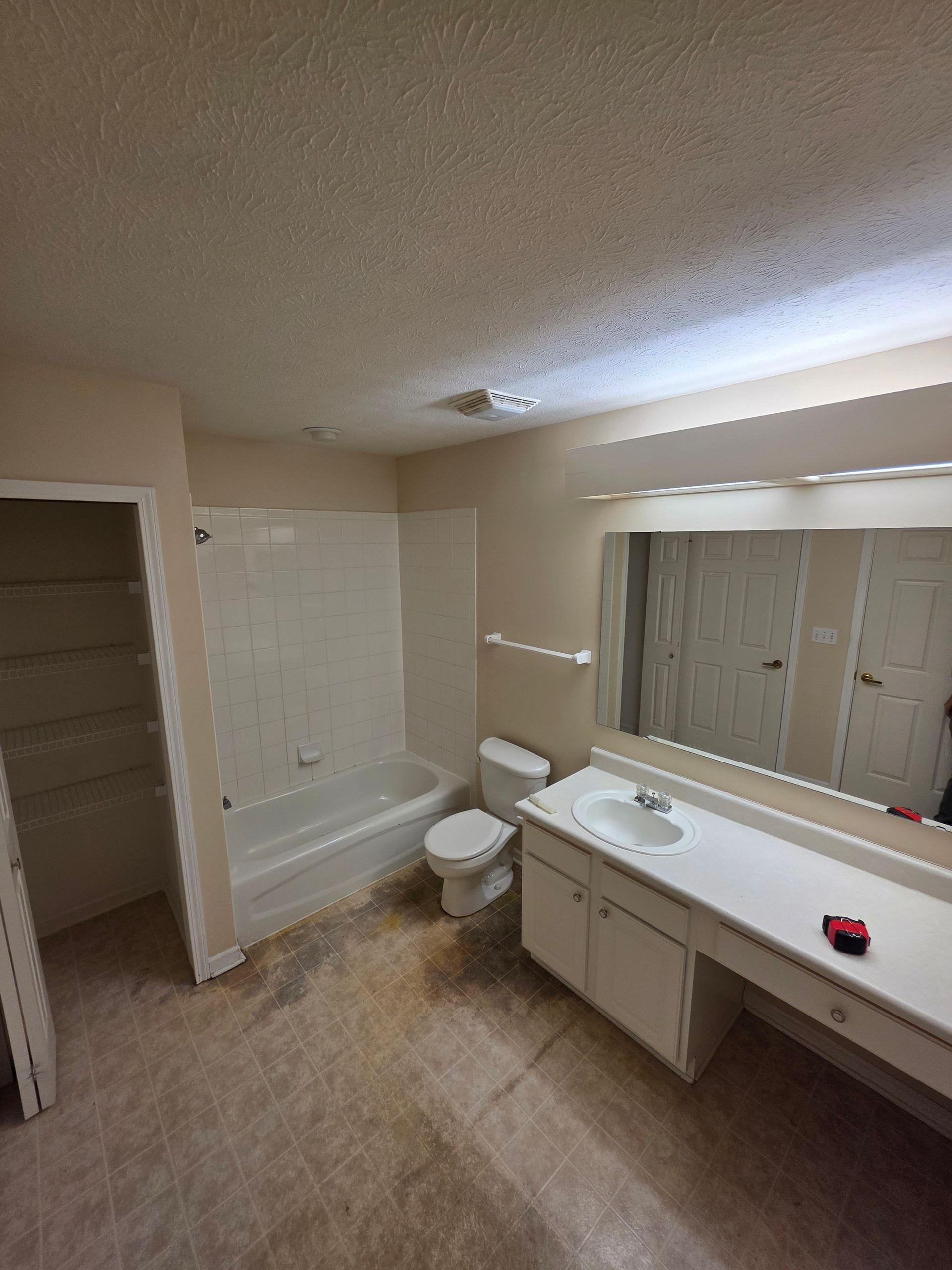 Bathroom with a white tub, toilet, and vanity, and a large mirror. Brown floor.