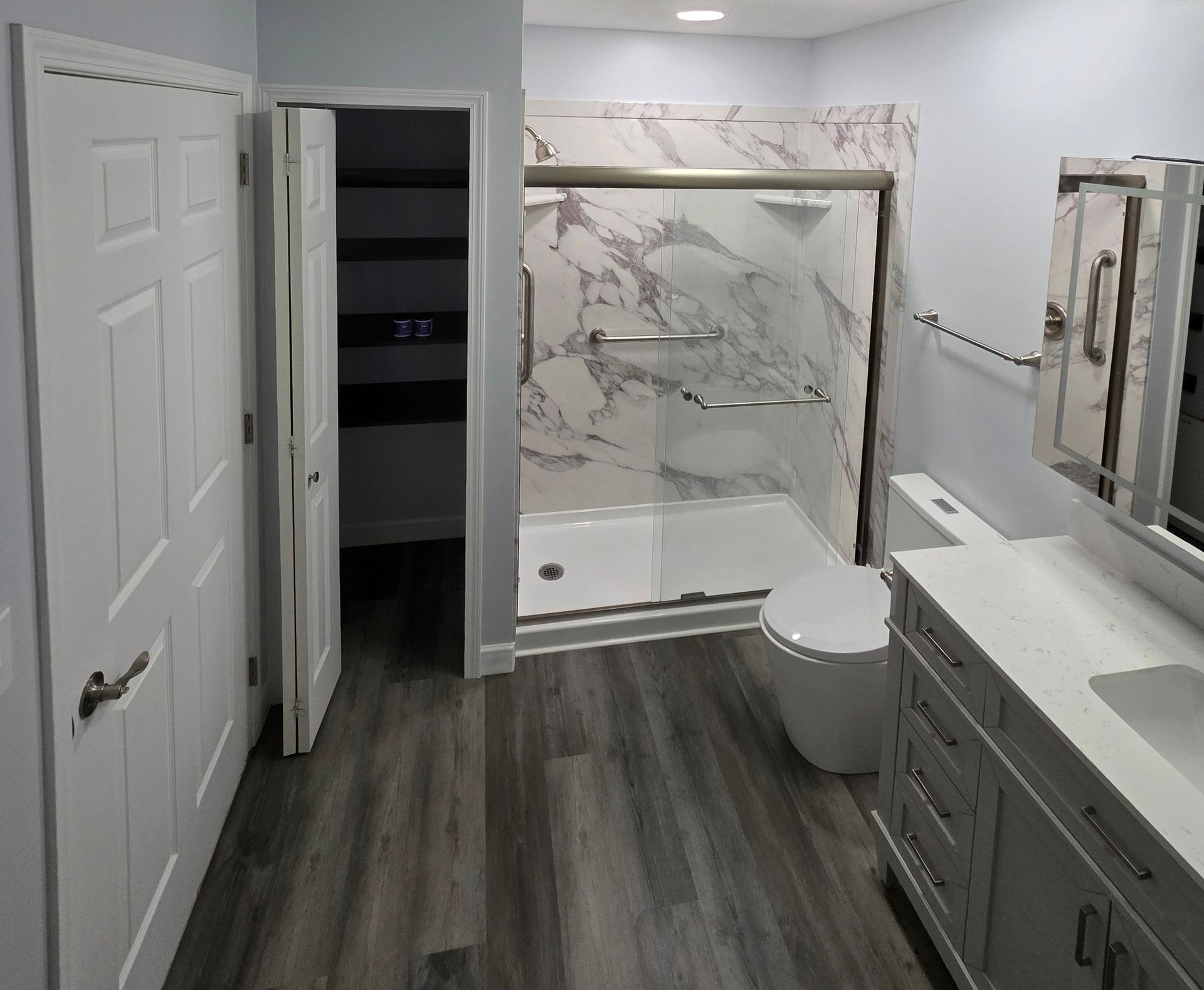 Bathroom with white vanity, marble shower, and gray wood-look flooring.