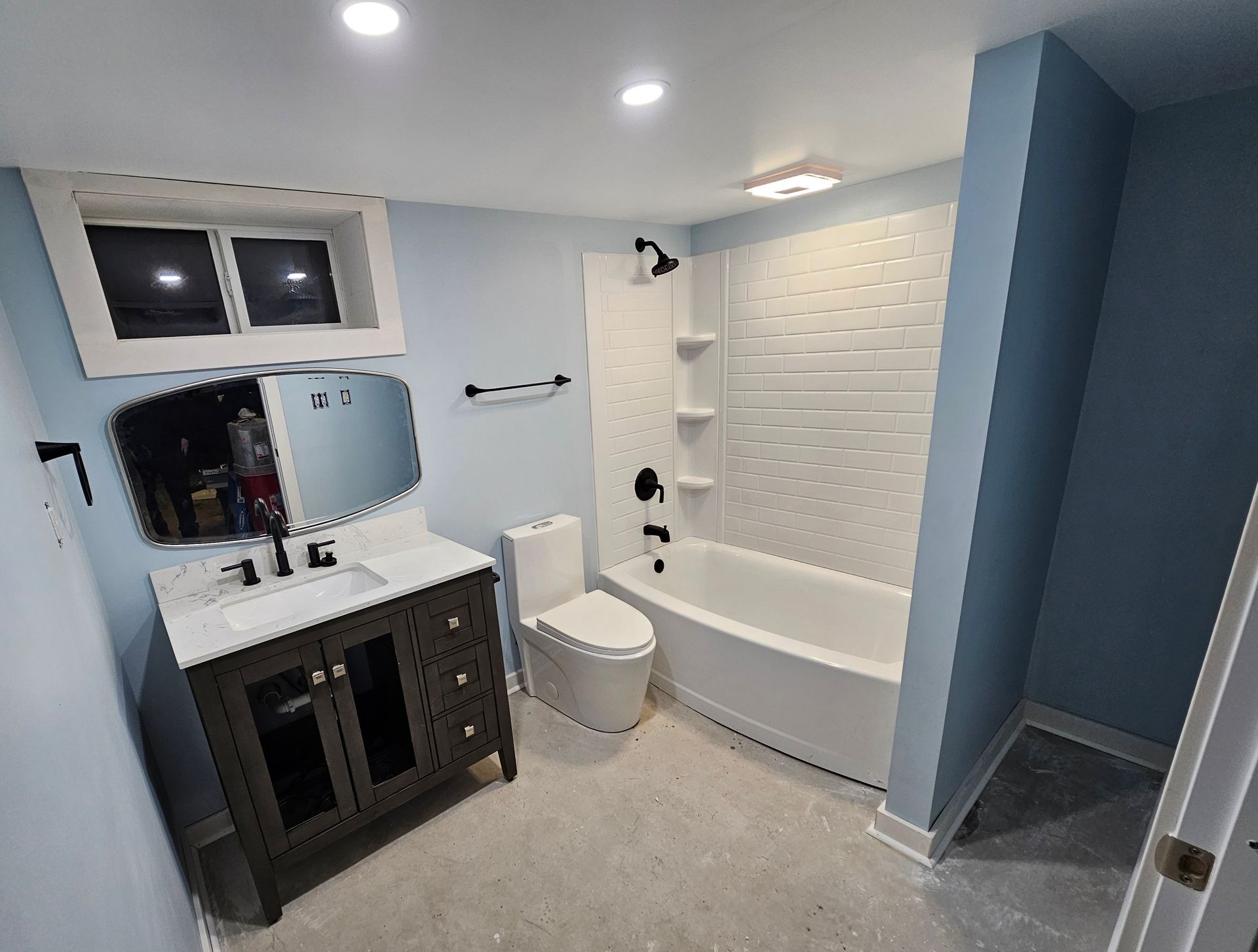 Newly renovated bathroom with blue walls, white bathtub and toilet, and dark wooden vanity.