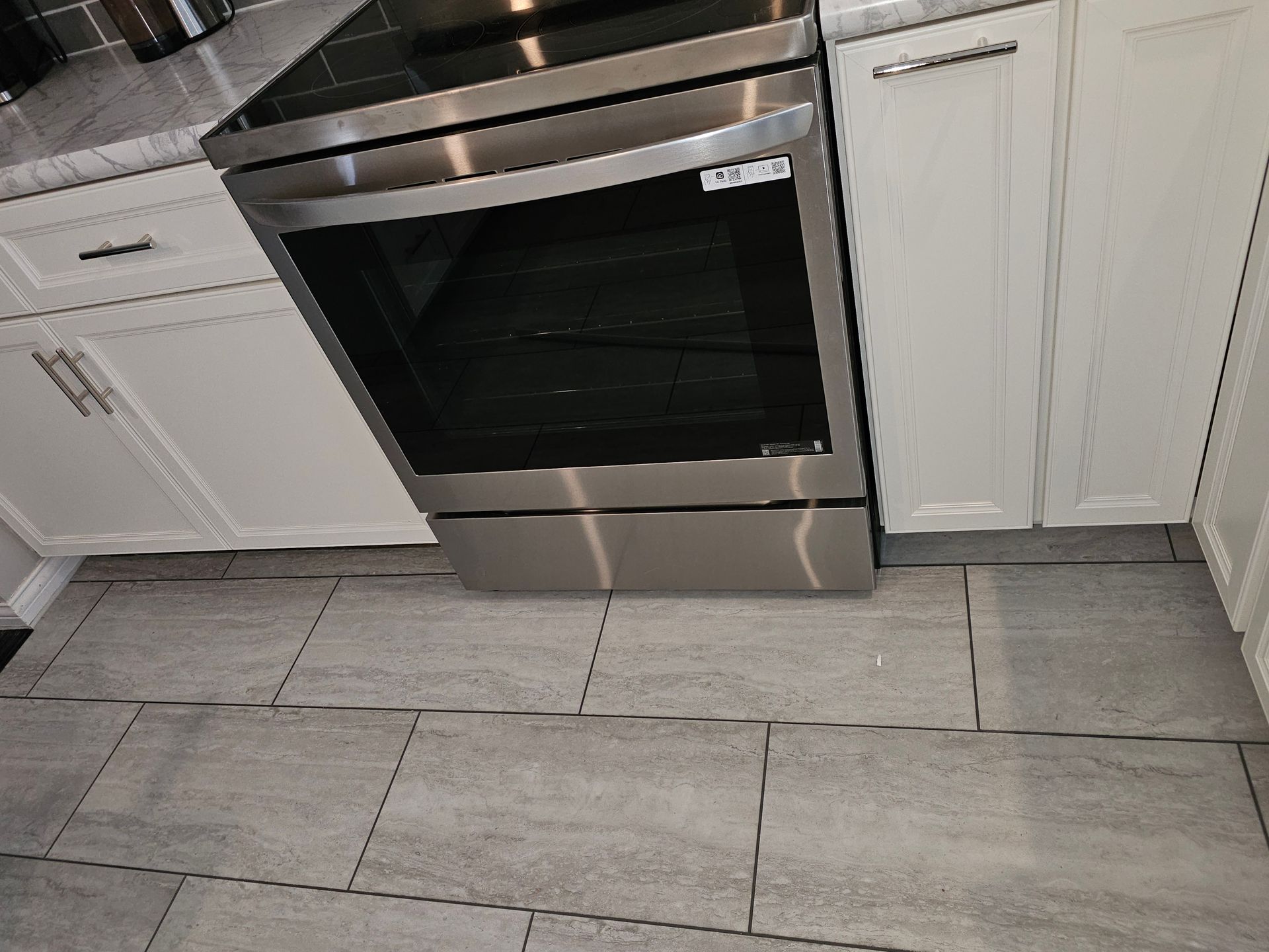 Stainless steel oven in a kitchen with white cabinets and gray tiled floor.