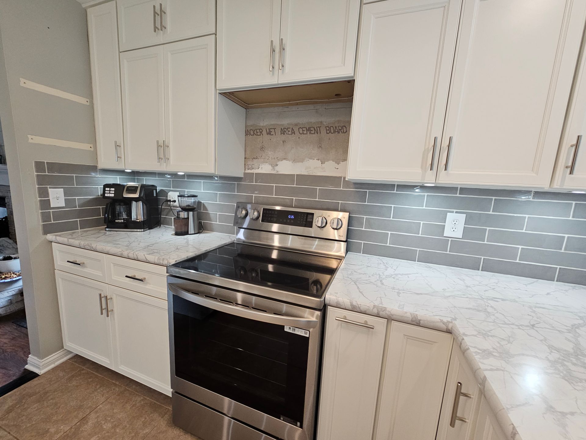 White kitchen cabinets, gray tile backsplash, stainless steel stove, and marble countertops.
