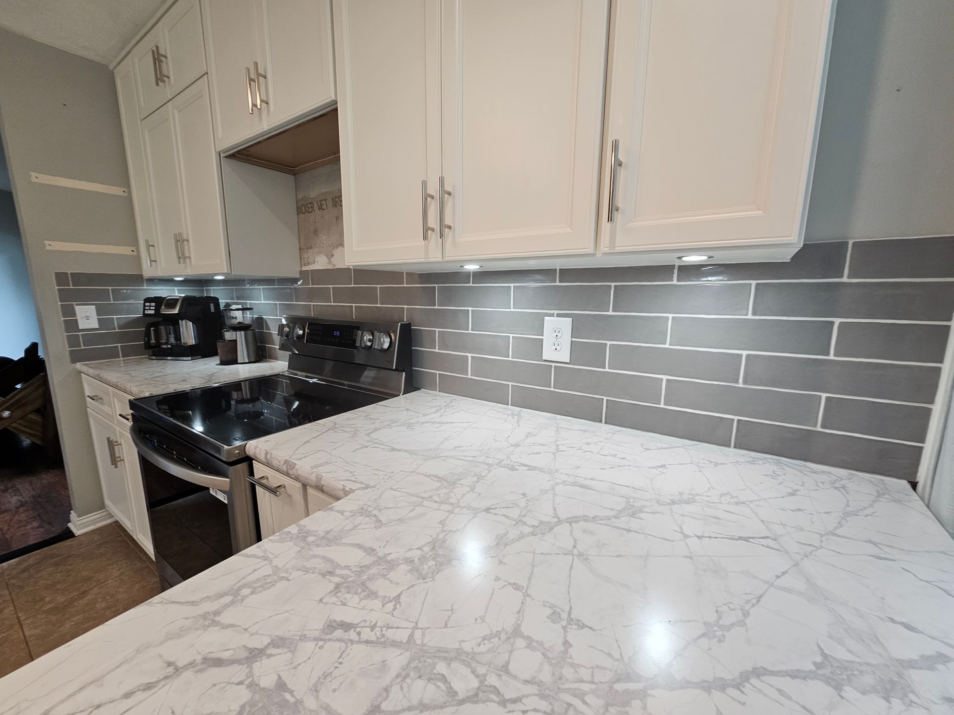 Kitchen with gray subway tile backsplash, white cabinets, and white marble-look countertops.