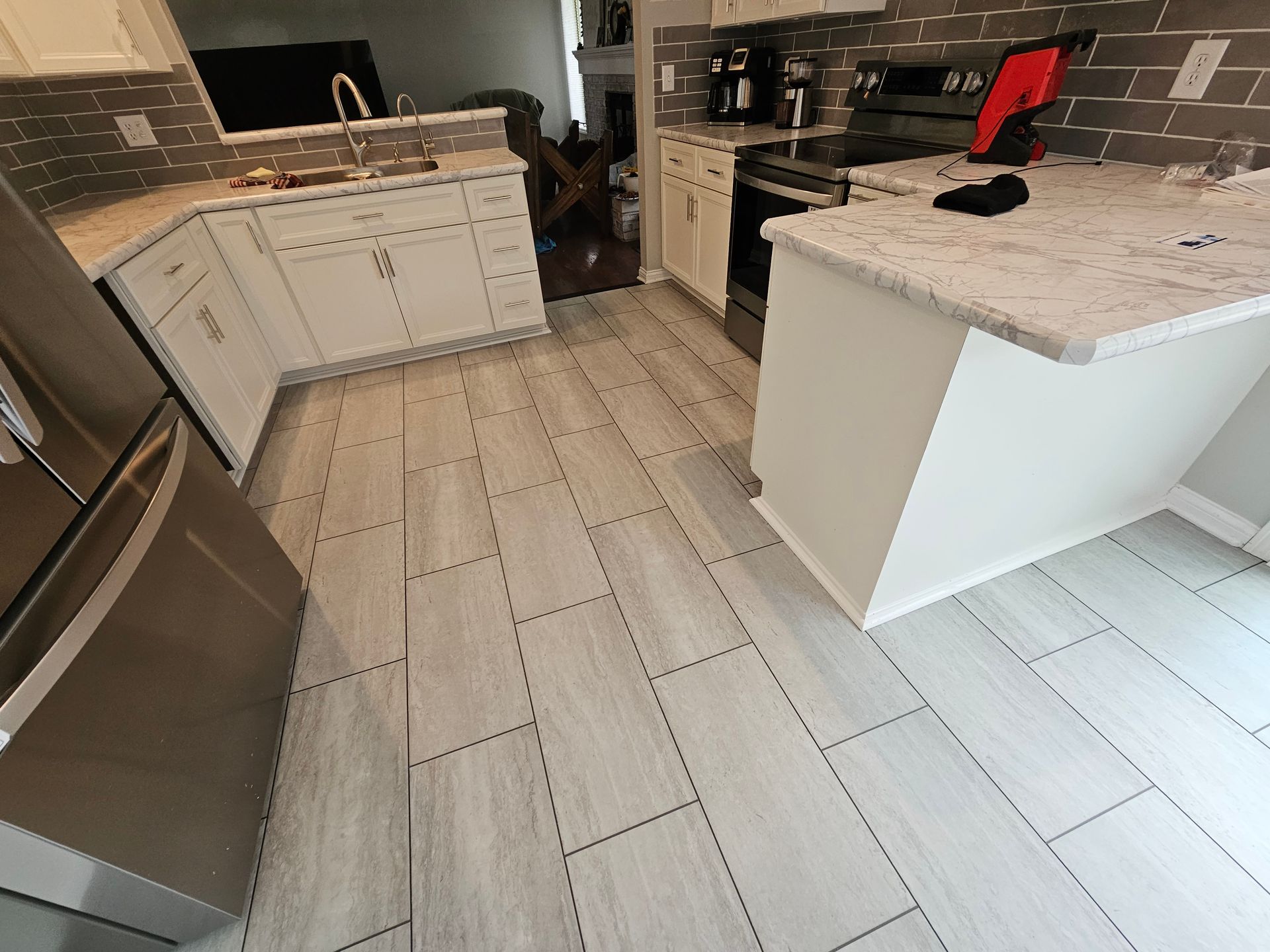 Kitchen with white cabinets, gray tile floor, stainless steel fridge, and a countertop island.