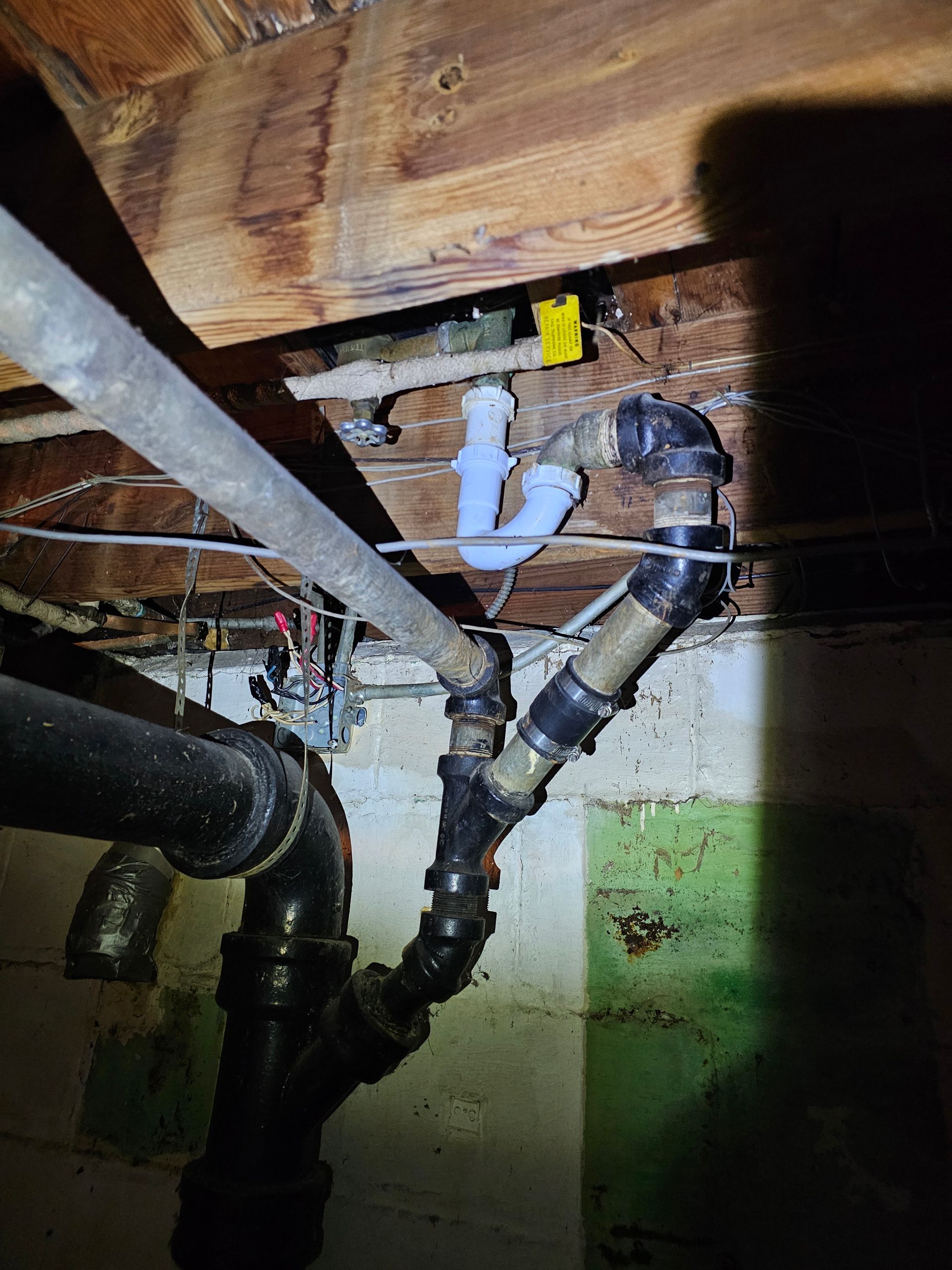 Plumbing pipes in a basement. Black cast iron and white plastic pipes connect overhead and to the floor.