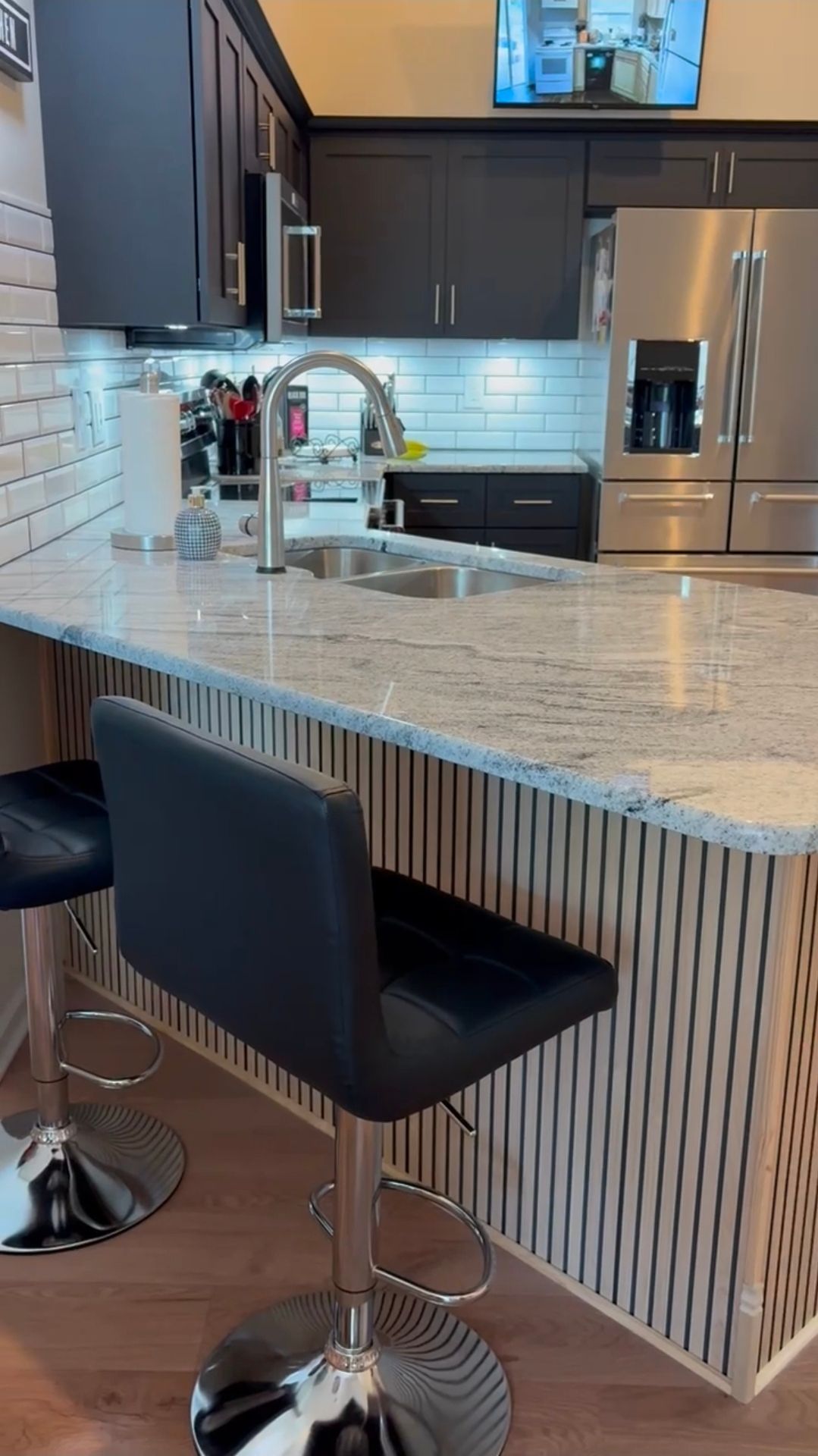 Kitchen with black cabinets, white countertop, stainless steel appliances, and two black bar stools.