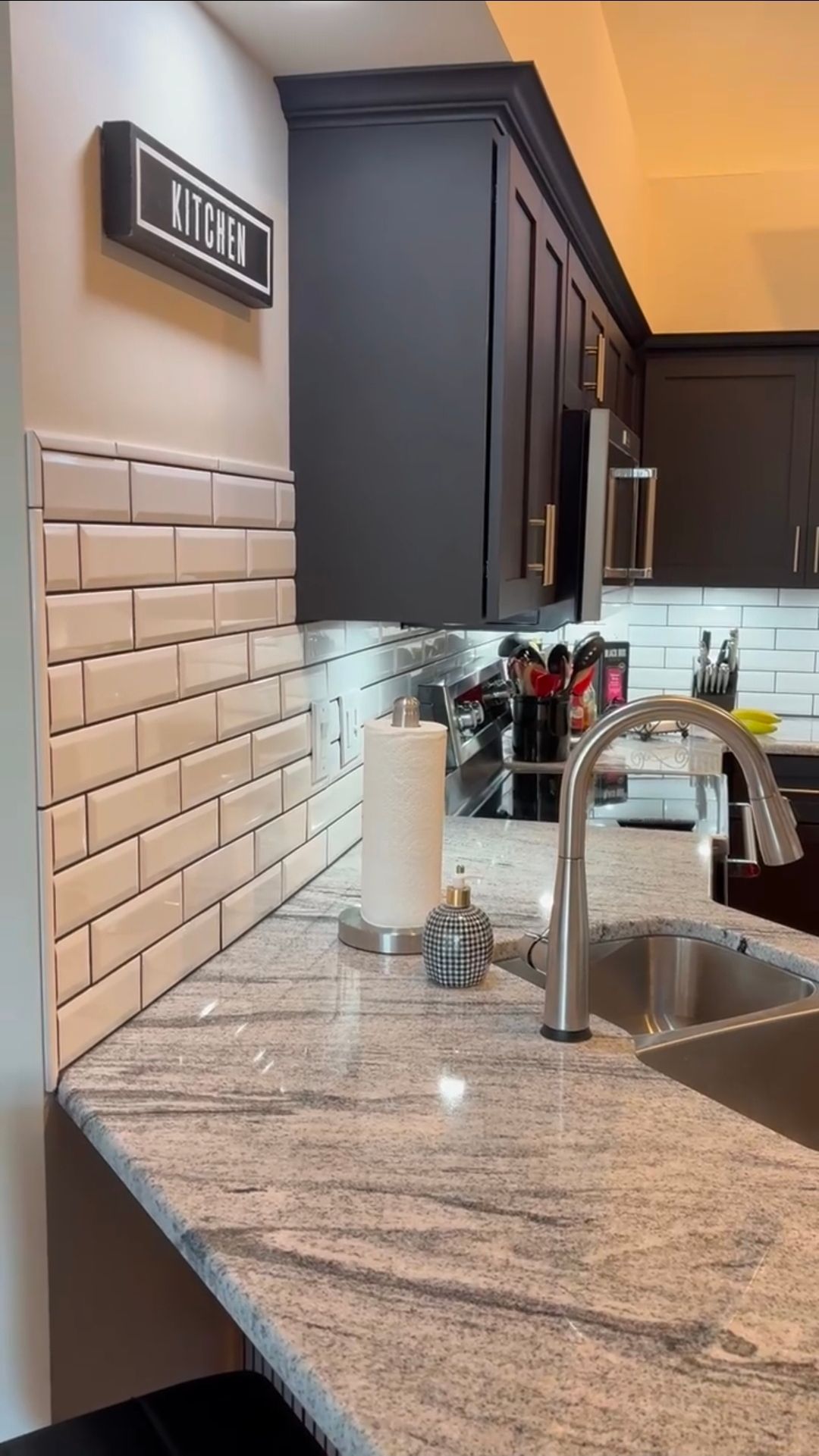 Kitchen with gray cabinets, white tile backsplash, granite countertop, and silver faucet.