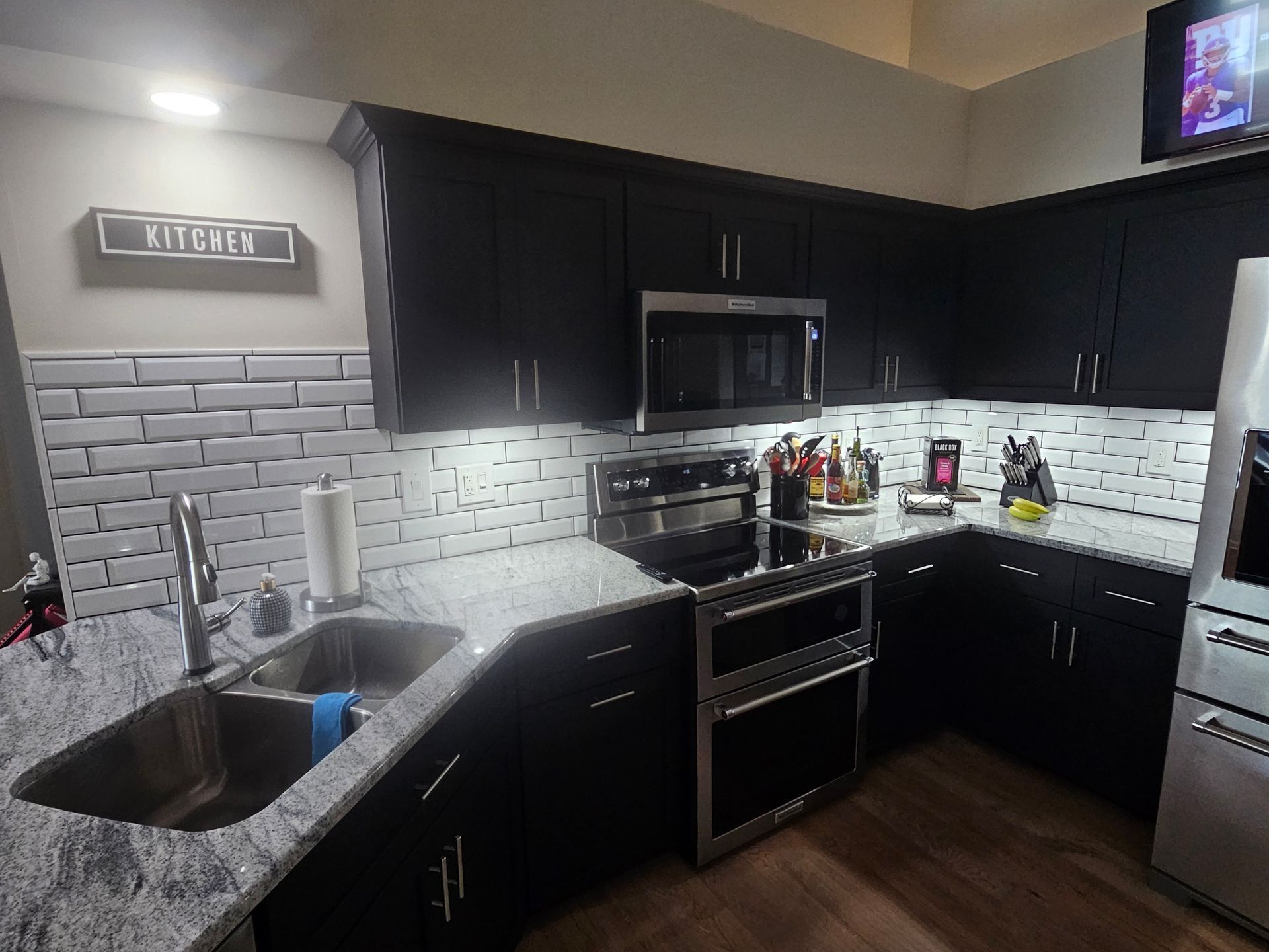 Black and white modern kitchen with stainless steel appliances, white subway tile backsplash, and dark cabinets.