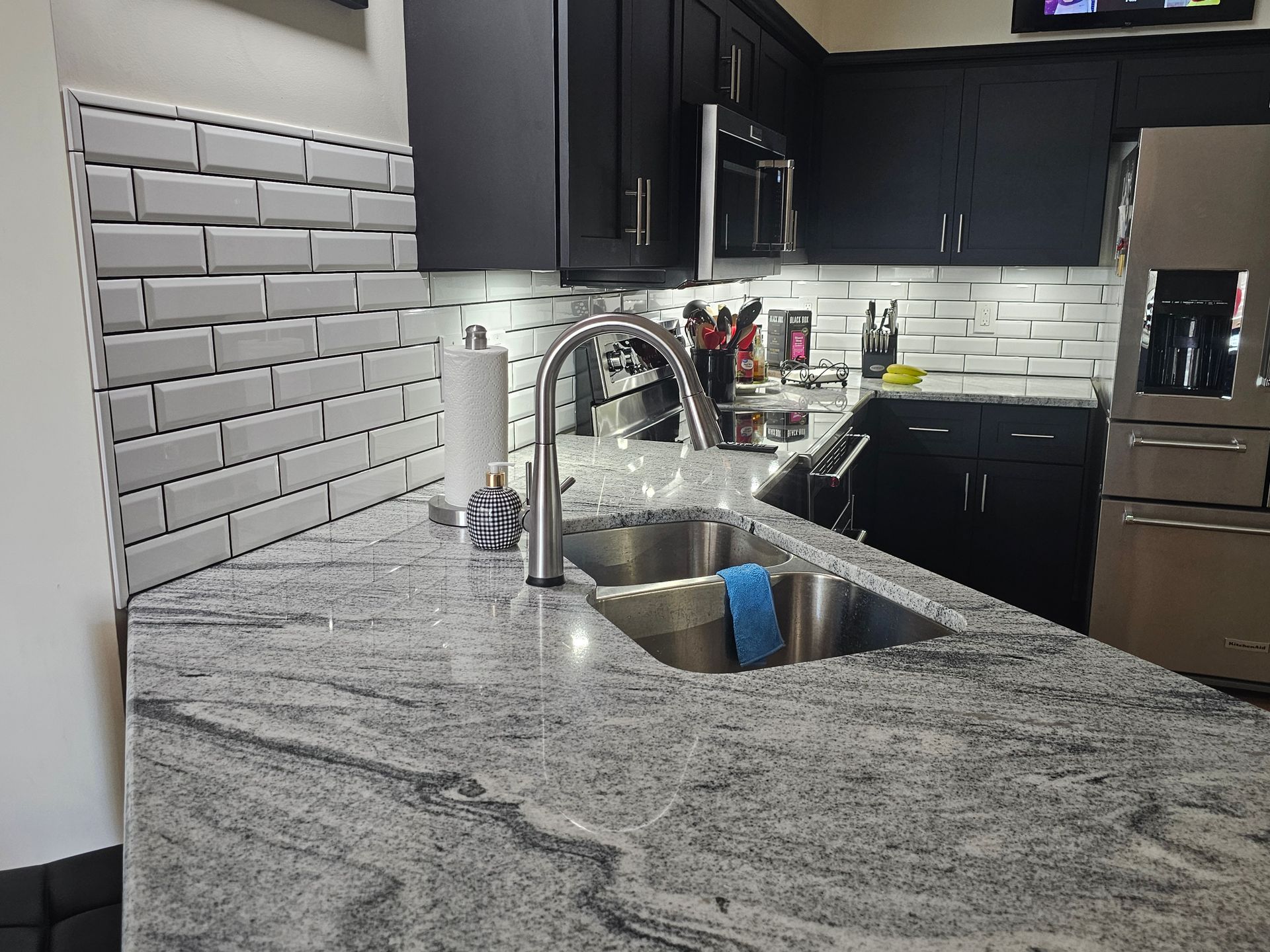 Kitchen with black cabinets, stainless steel appliances, and gray granite countertops. White subway tile backsplash.