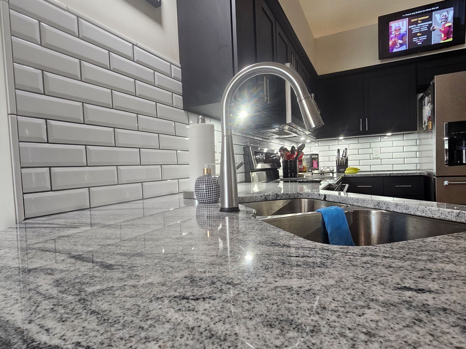 Kitchen with stainless steel sink, granite countertop, white subway tile backsplash, and dark cabinets.