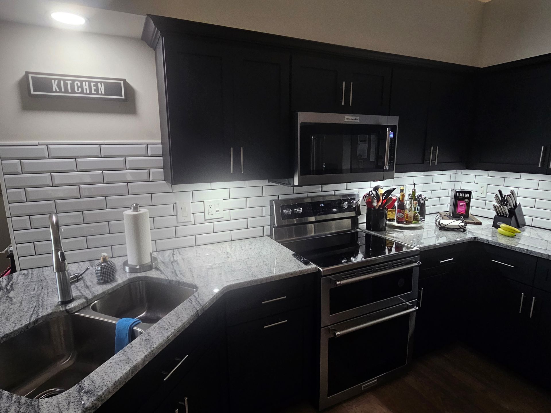 Black kitchen cabinets with granite countertops, stainless steel appliances, and subway tile backsplash.