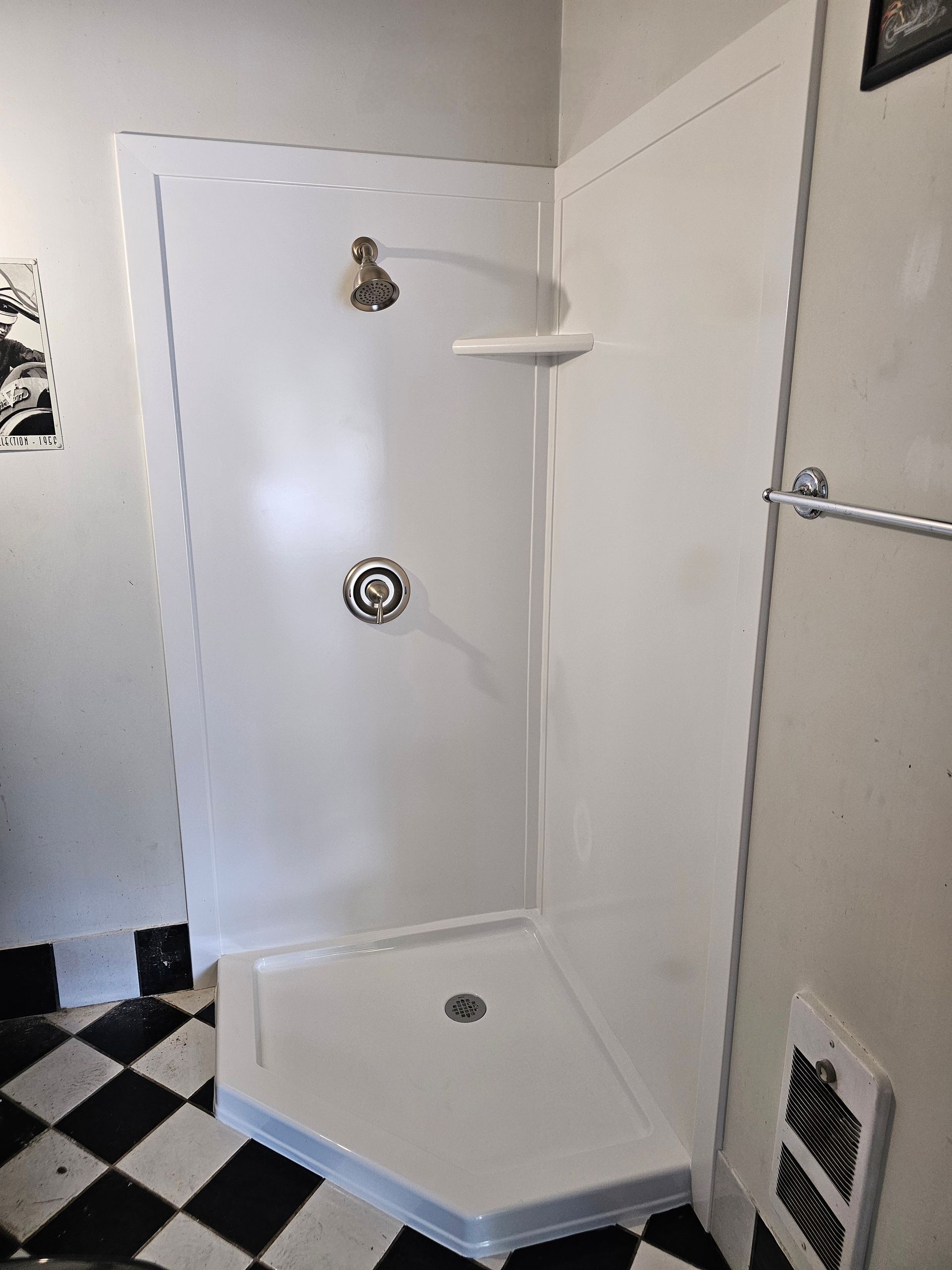 White corner shower with gold fixtures and black and white tiled floor.