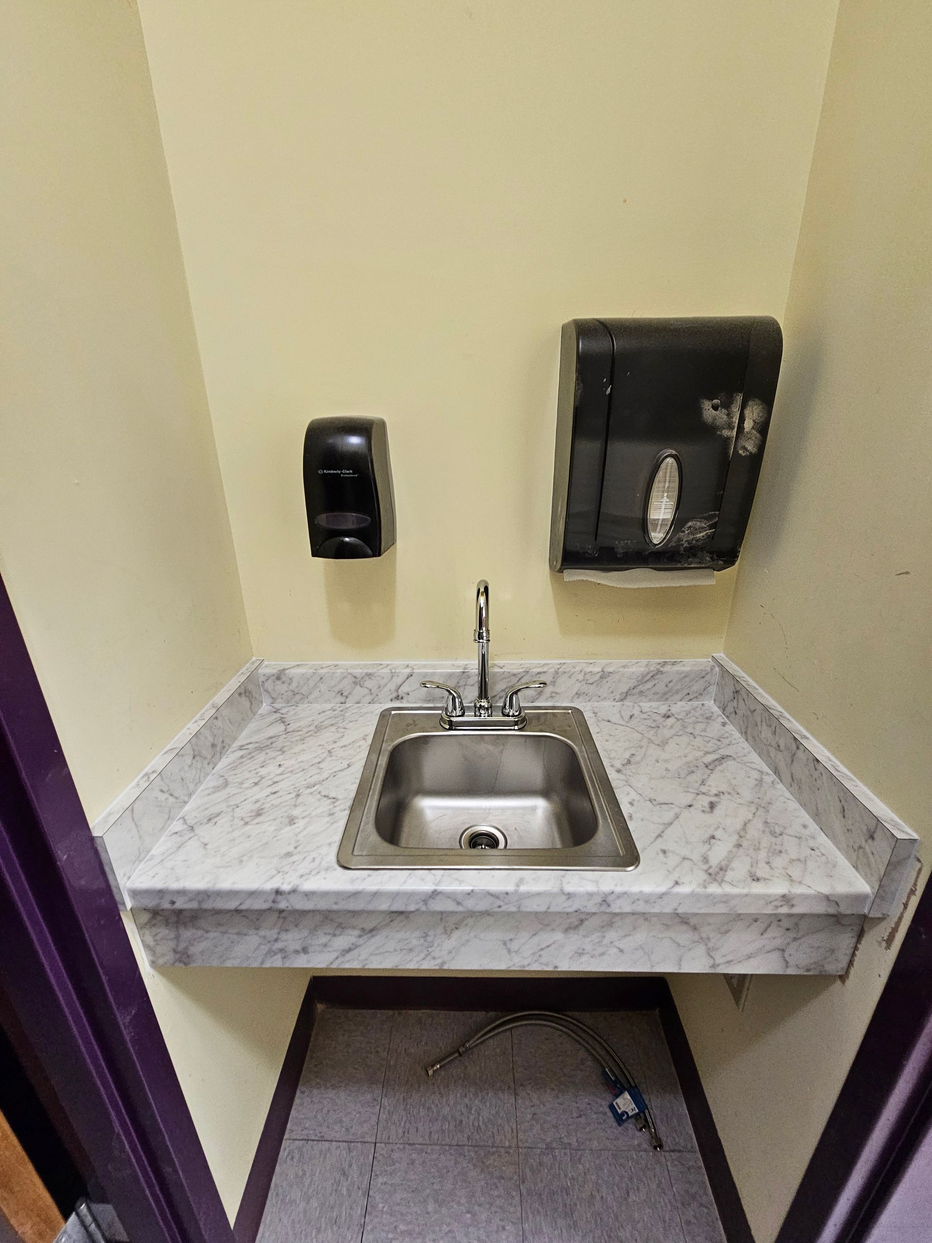 Small public restroom sink with countertop, soap dispenser, and paper towel dispenser.
