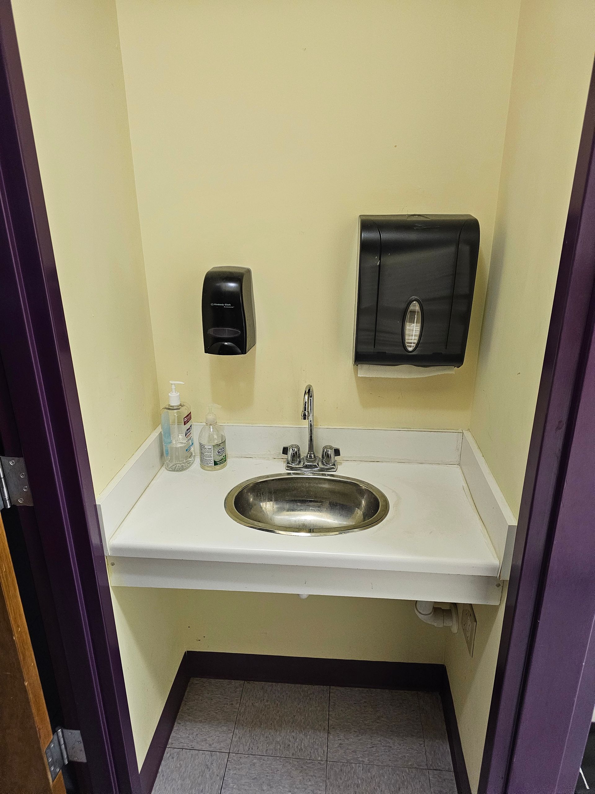 A small bathroom sink area, featuring a stainless steel basin, mounted soap dispenser, and paper towel dispenser.