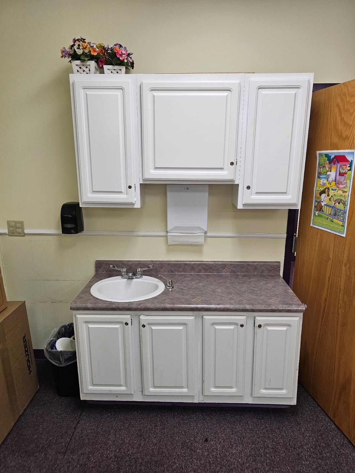 White cabinets and sink in a classroom. Paper towel dispenser and flowers above the sink.