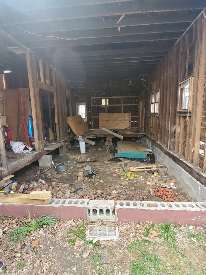 Interior of a partially demolished building; exposed wood framing, debris on the floor, and a damaged foundation.