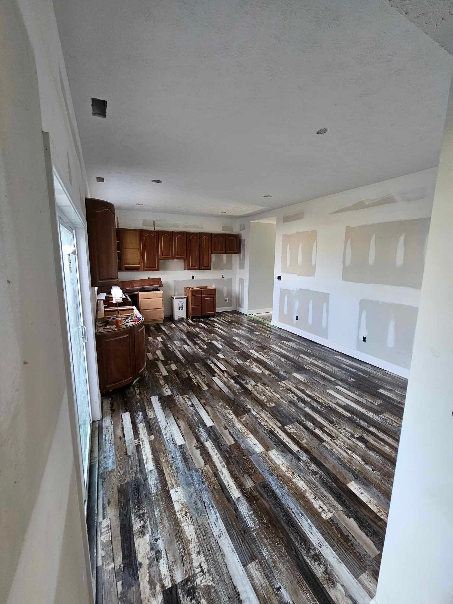 Interior of a room with unfinished drywall and dark wood flooring; kitchen cabinets in the background.