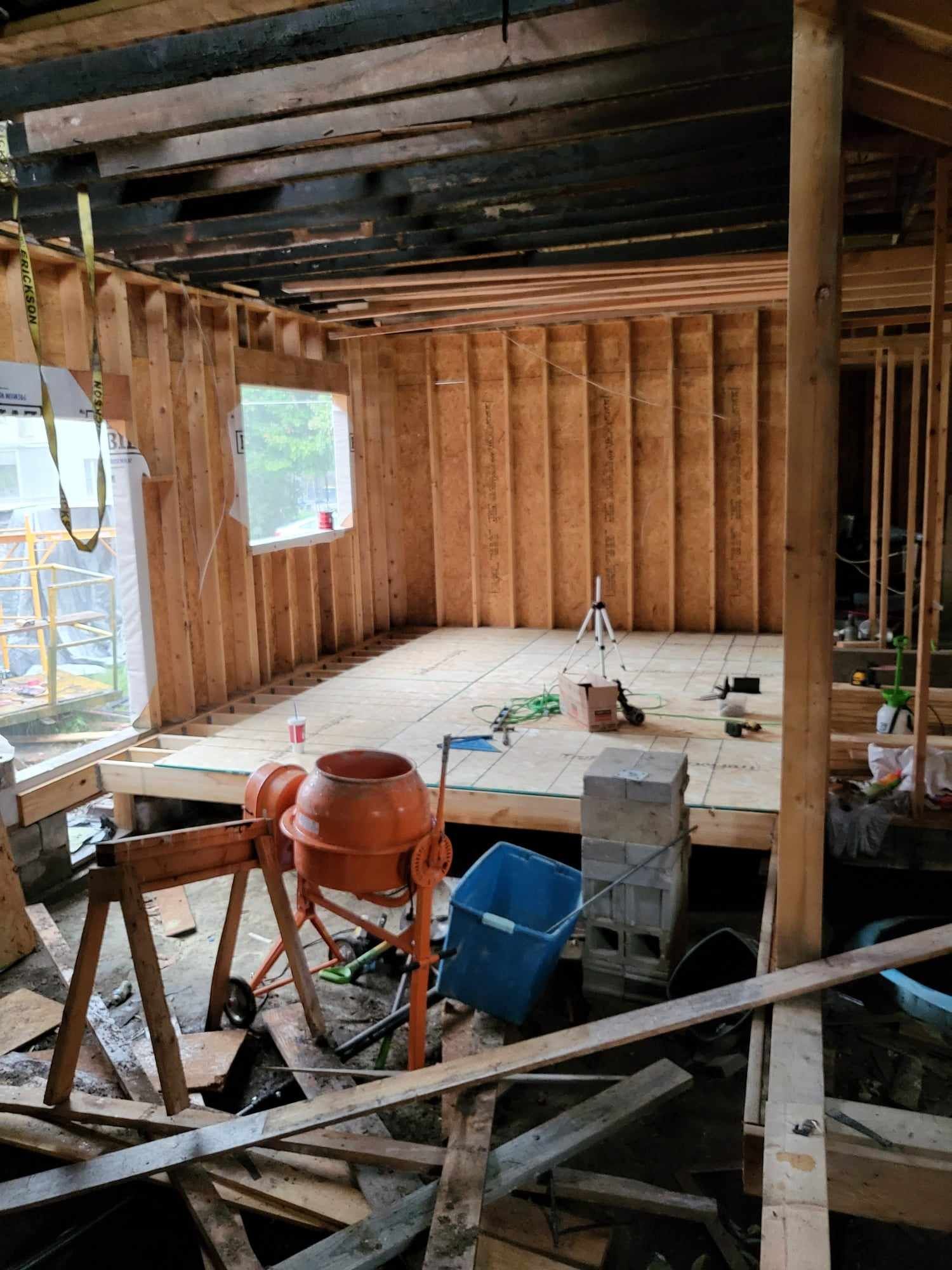 Interior of a room under construction, with wooden framing, flooring, and a cement mixer.