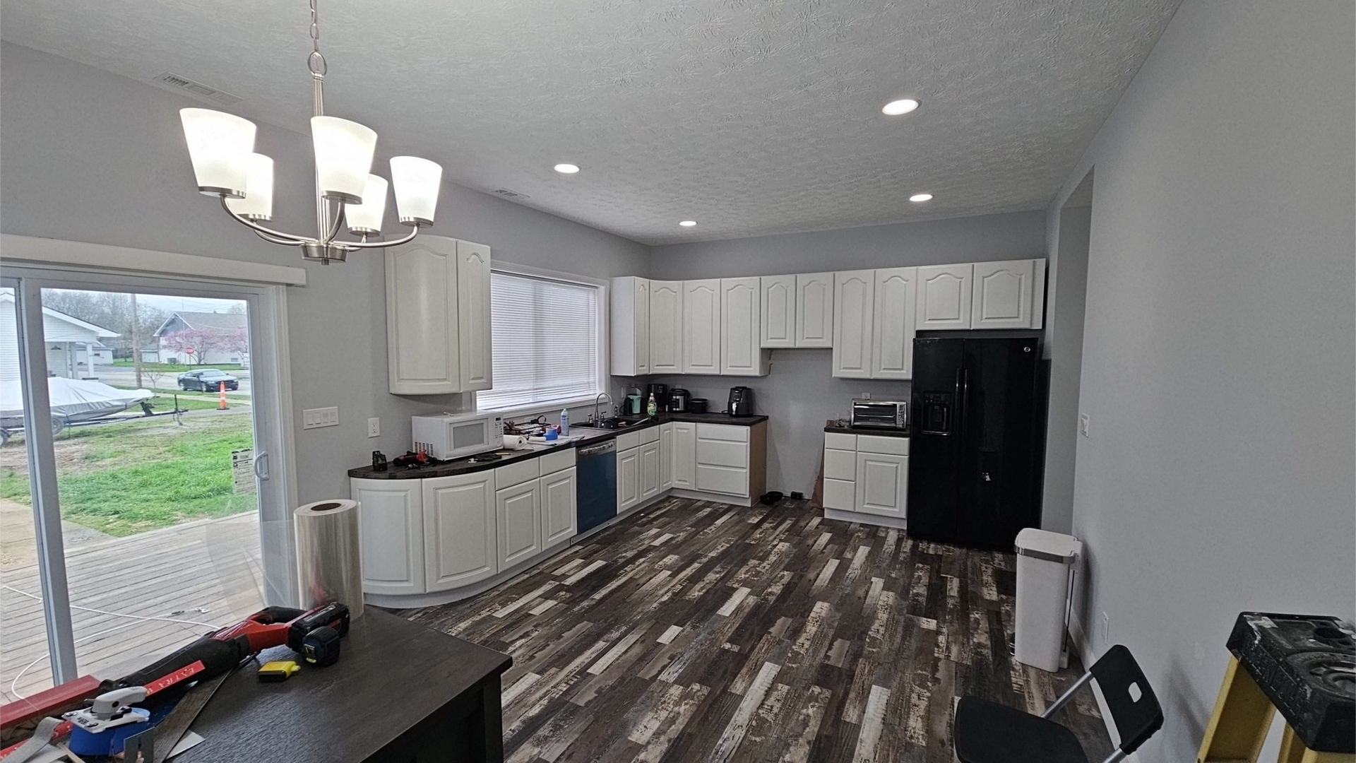 Kitchen with white cabinets, black appliances, dark wood-look floor, and a chandelier.