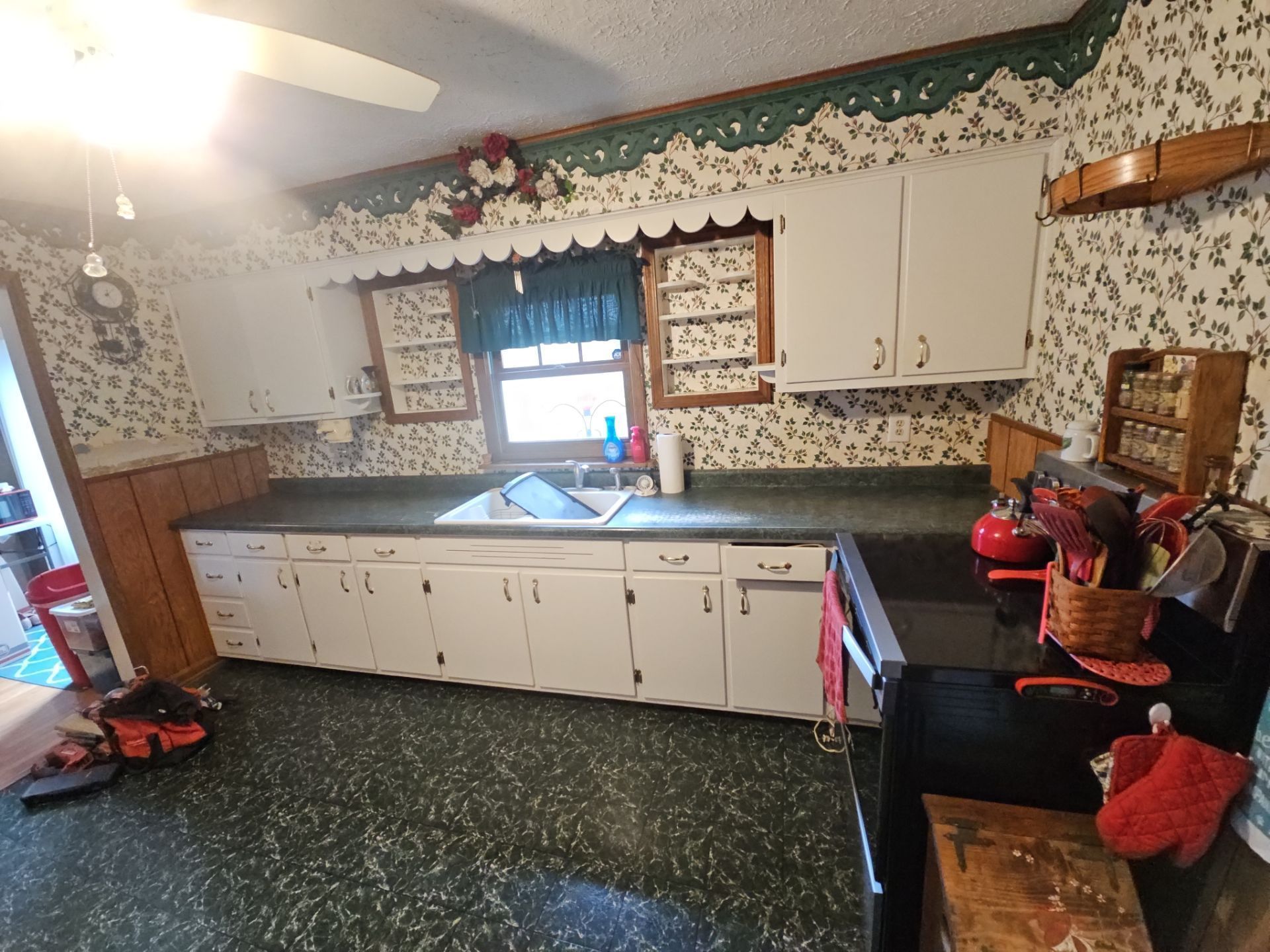 Kitchen with white cabinets, green countertop, floral wallpaper, and green flooring.
