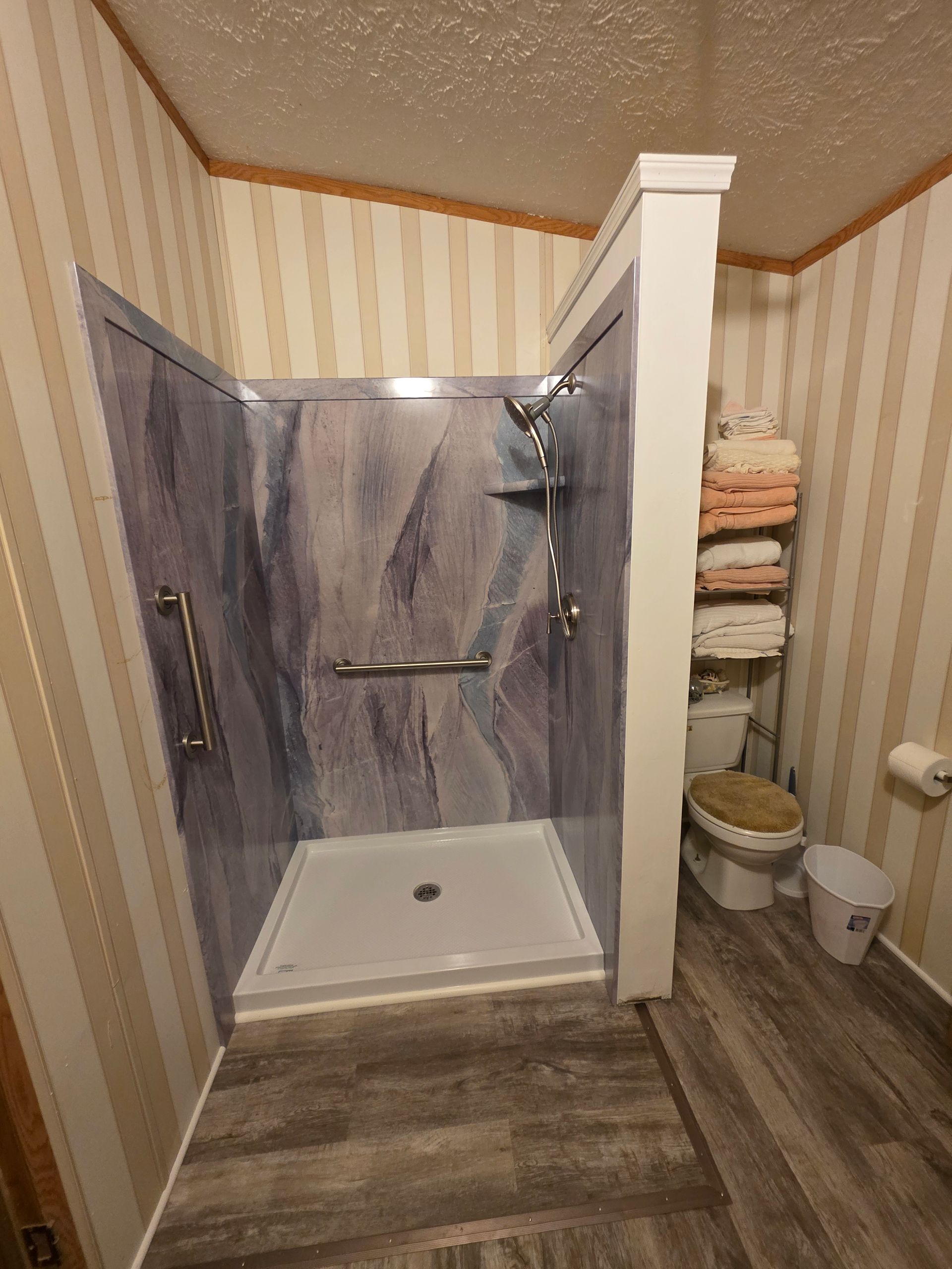 Accessible shower stall with grab bars and hand shower in a bathroom with striped wallpaper and a stack of towels.