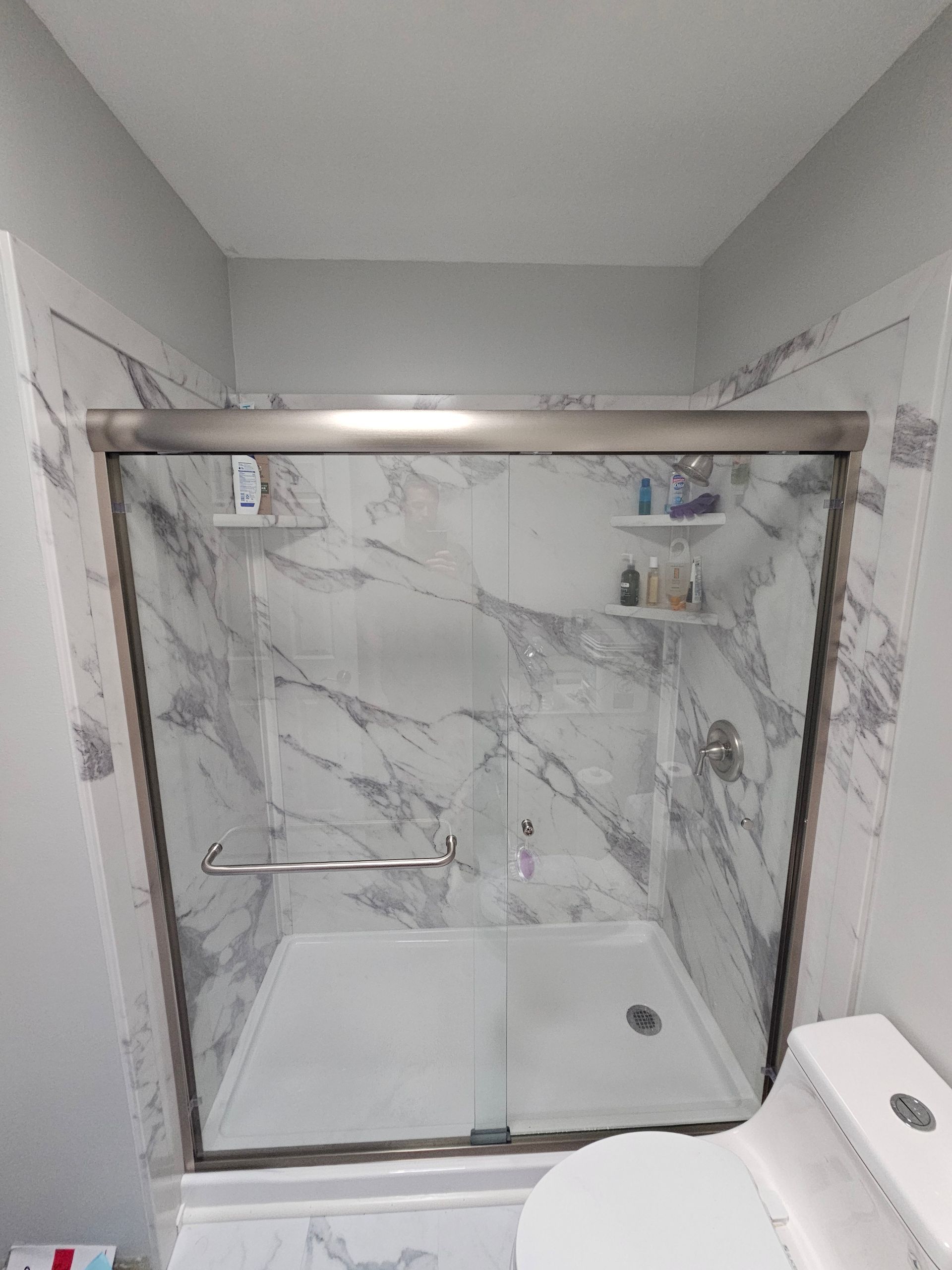 Shower stall with glass doors and marble-look walls. Includes a grab bar and shelves with toiletries.