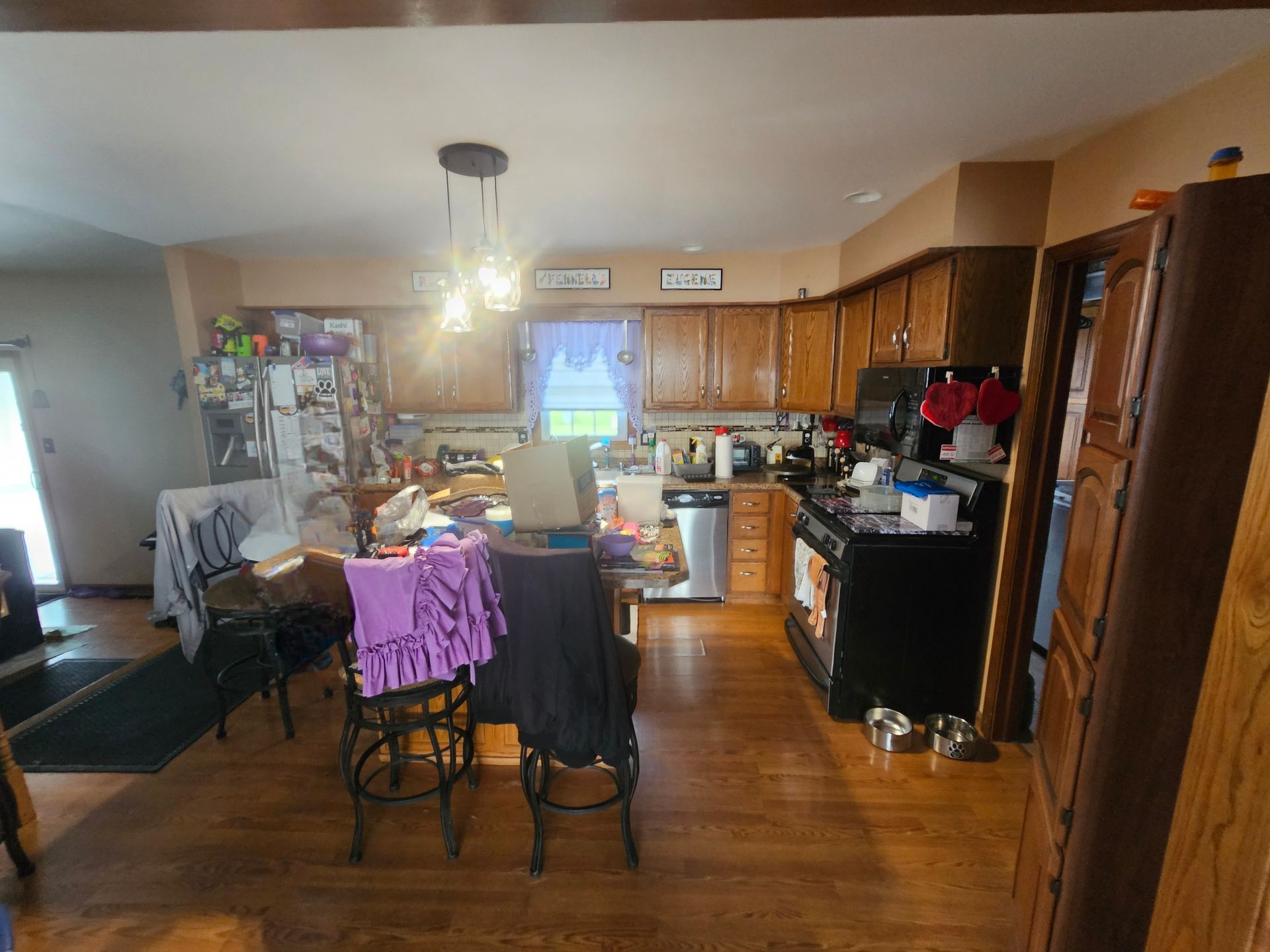 Kitchen with wood cabinets, black appliances, table with stools, and pendant lights.