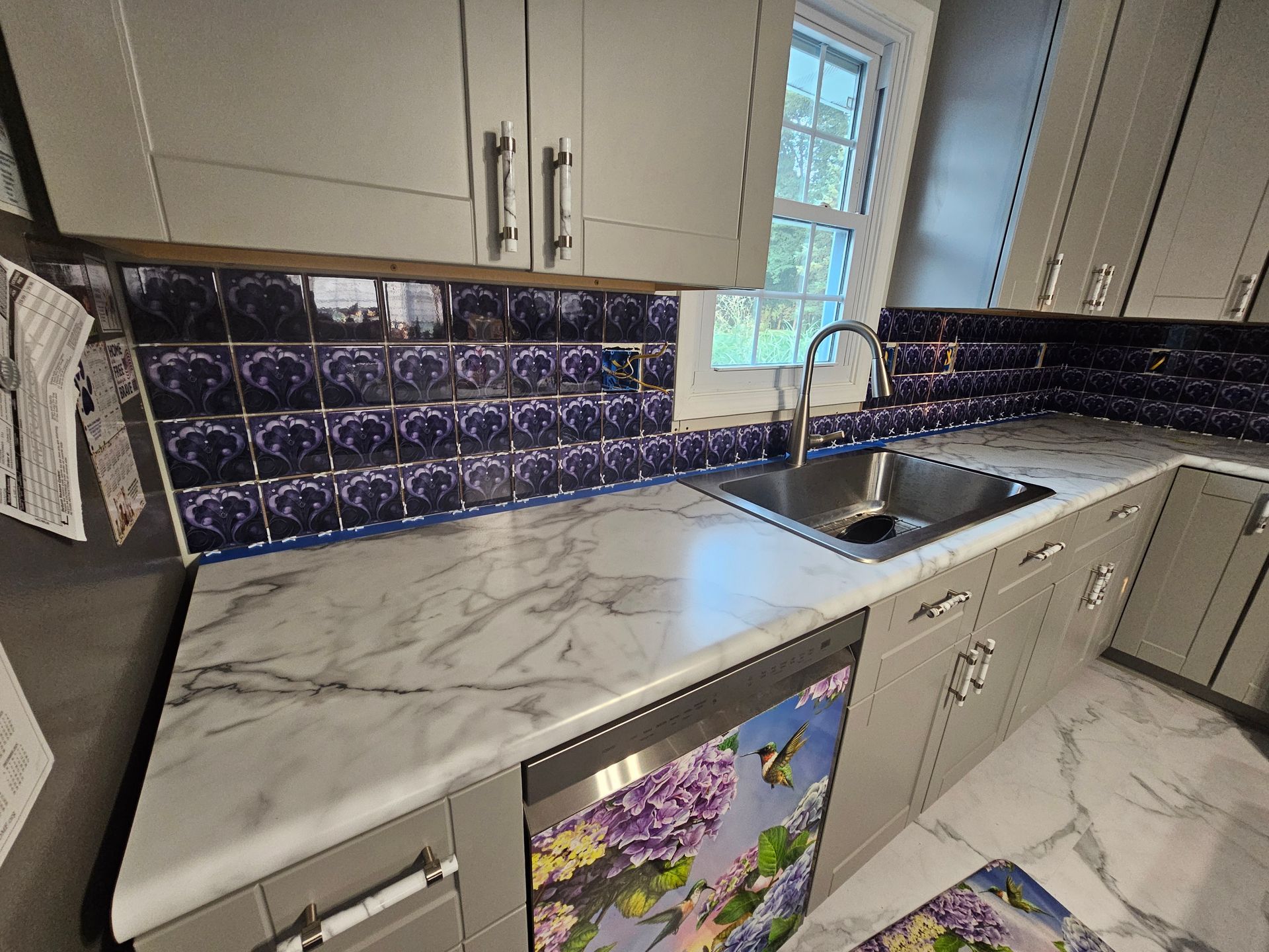 Gray kitchen with white marble countertops, a stainless steel sink, and blue and purple tile backsplash.
