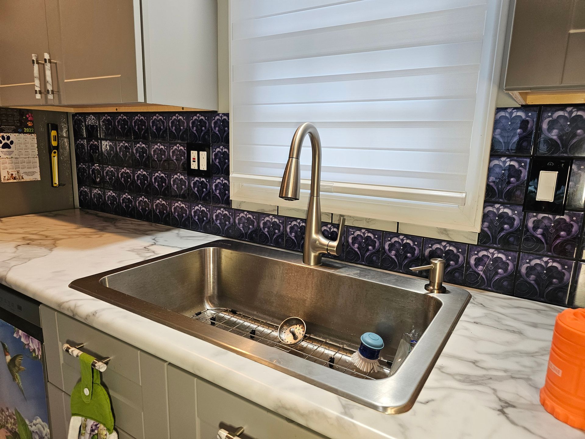 Stainless steel kitchen sink with faucet, marble countertop, and patterned backsplash.