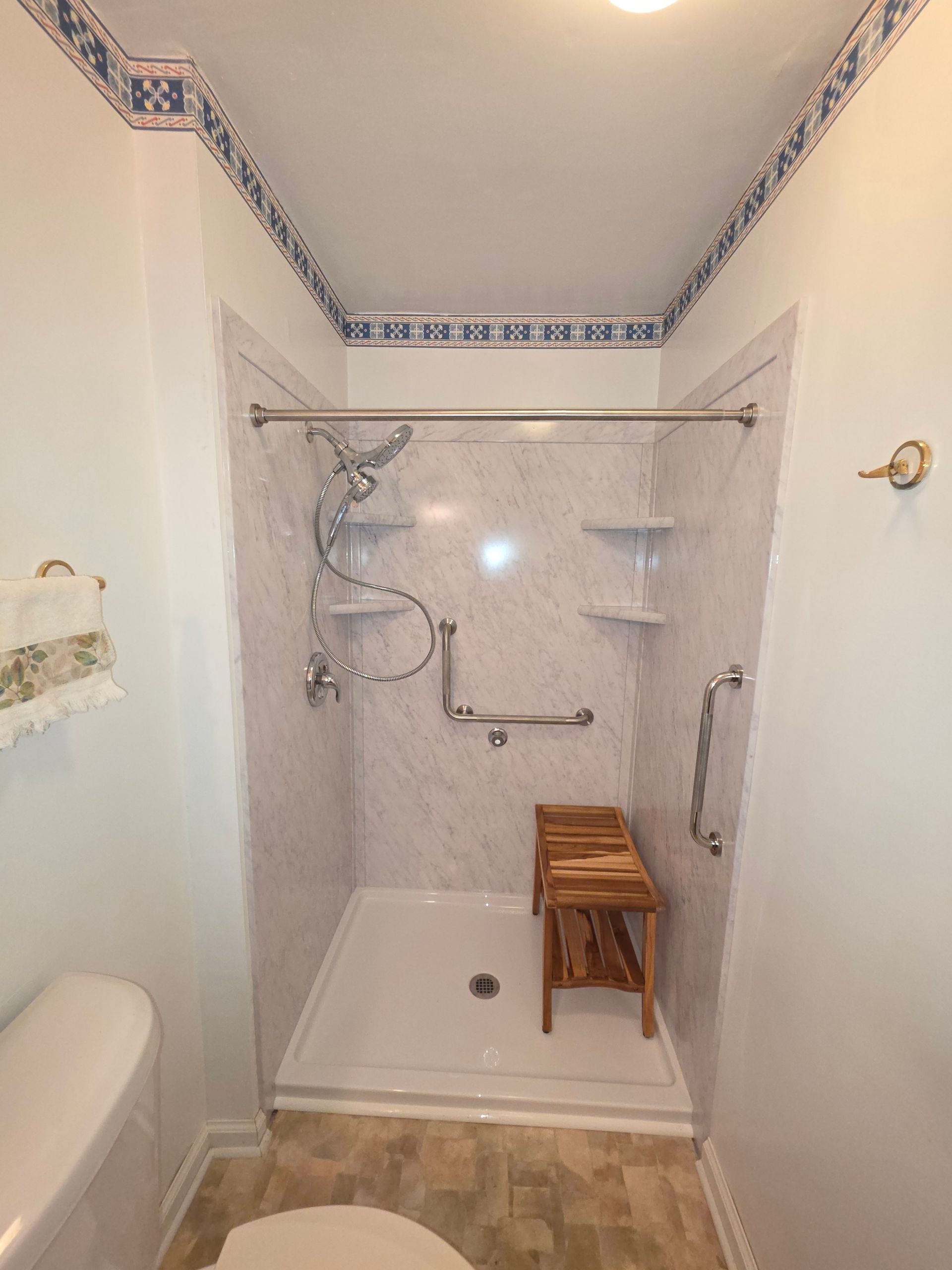 Accessible shower stall with grab bars, shower seat, and handheld showerhead in a bathroom.